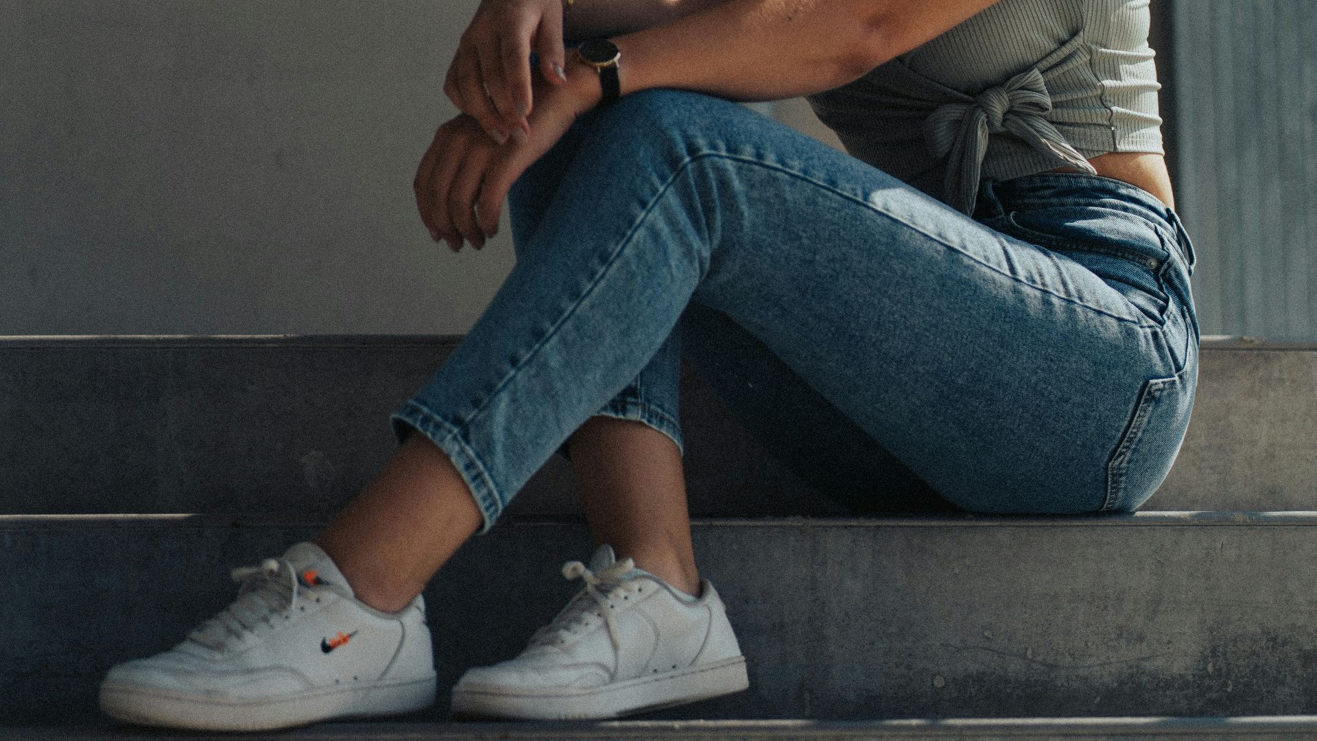 woman in gray t-shirt and blue denim jeans sitting on gray concrete stairs