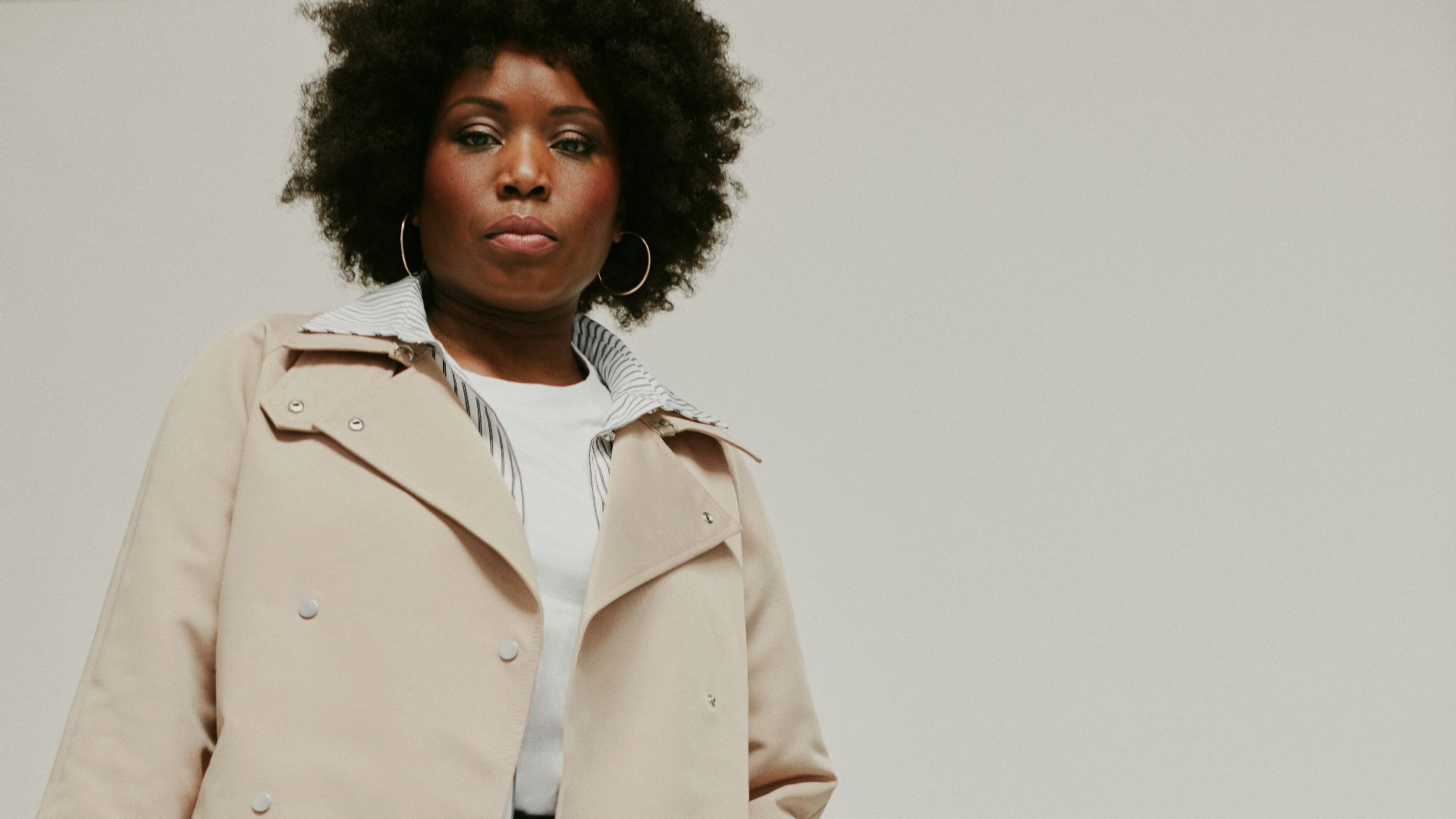 a woman in a trench coat holding a pink purse