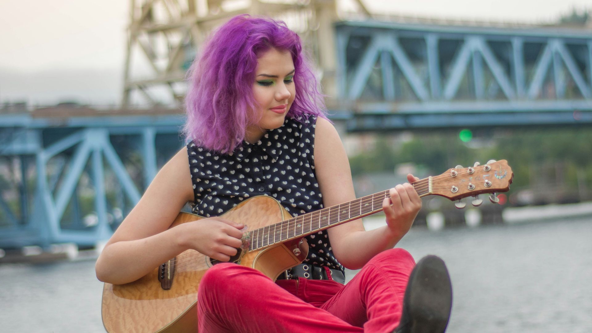 woman wearing black shirt sitting on grass while playing guitar