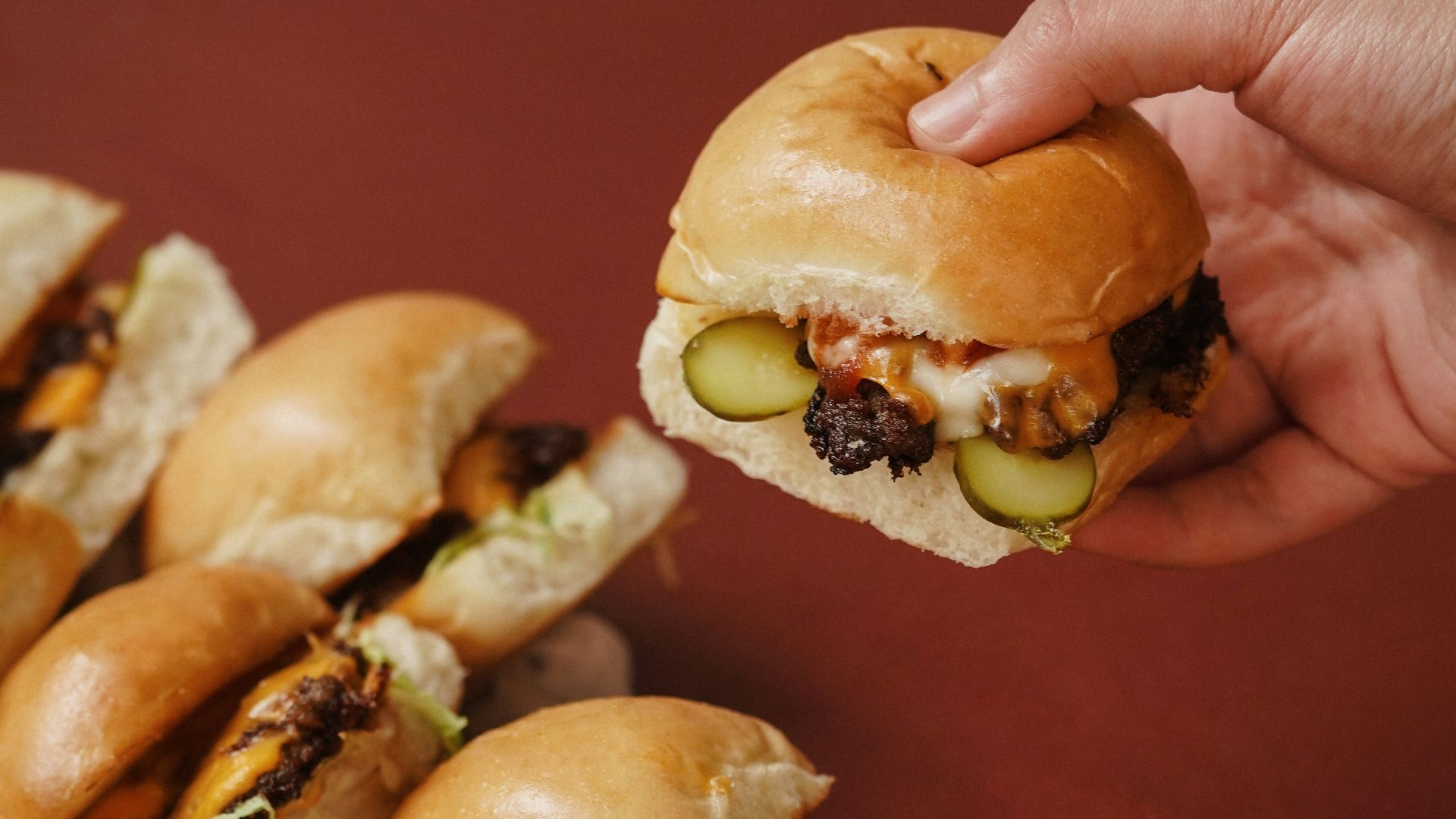 a hand holding a sandwich over a pile of mini sandwiches