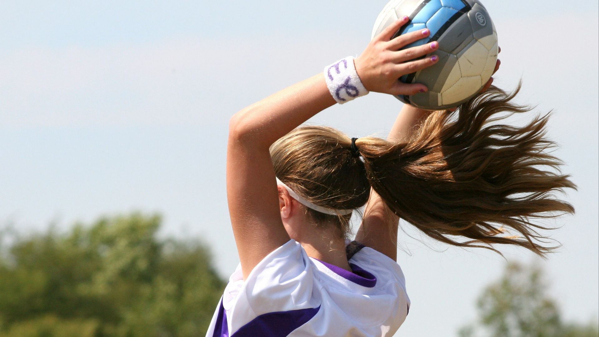 A woman in a purple and white uniform holding a white and blue ball