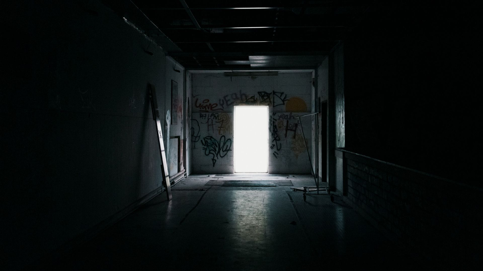 a dark hallway with a door and graffiti on the walls