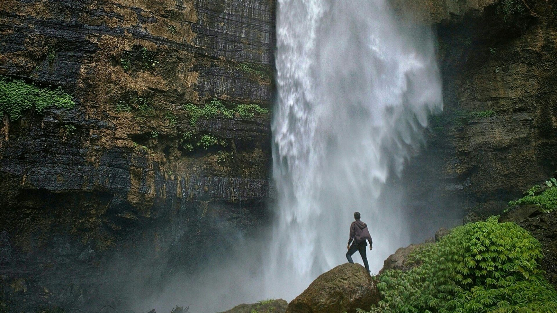 person standing on brown rock formation looking at waterfalls during daytime