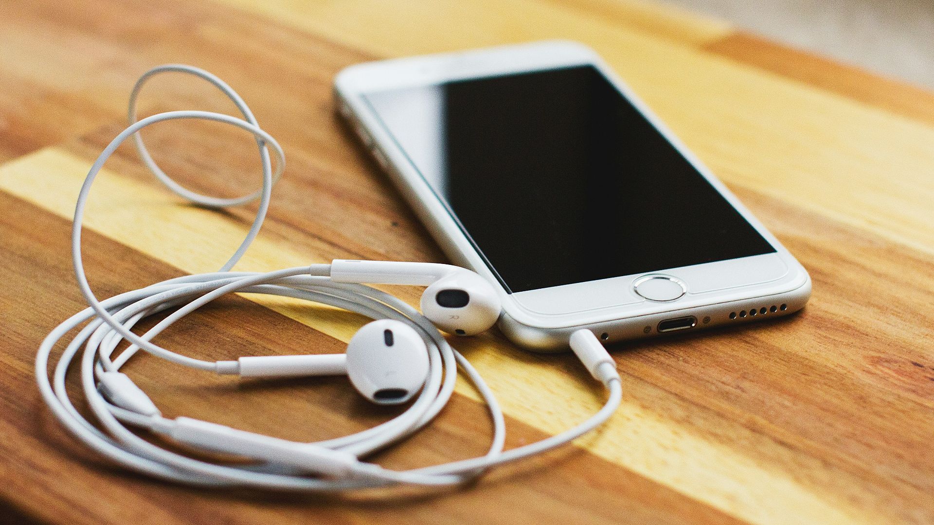 silver iPhone 6 with EarPods on brown wooden table
