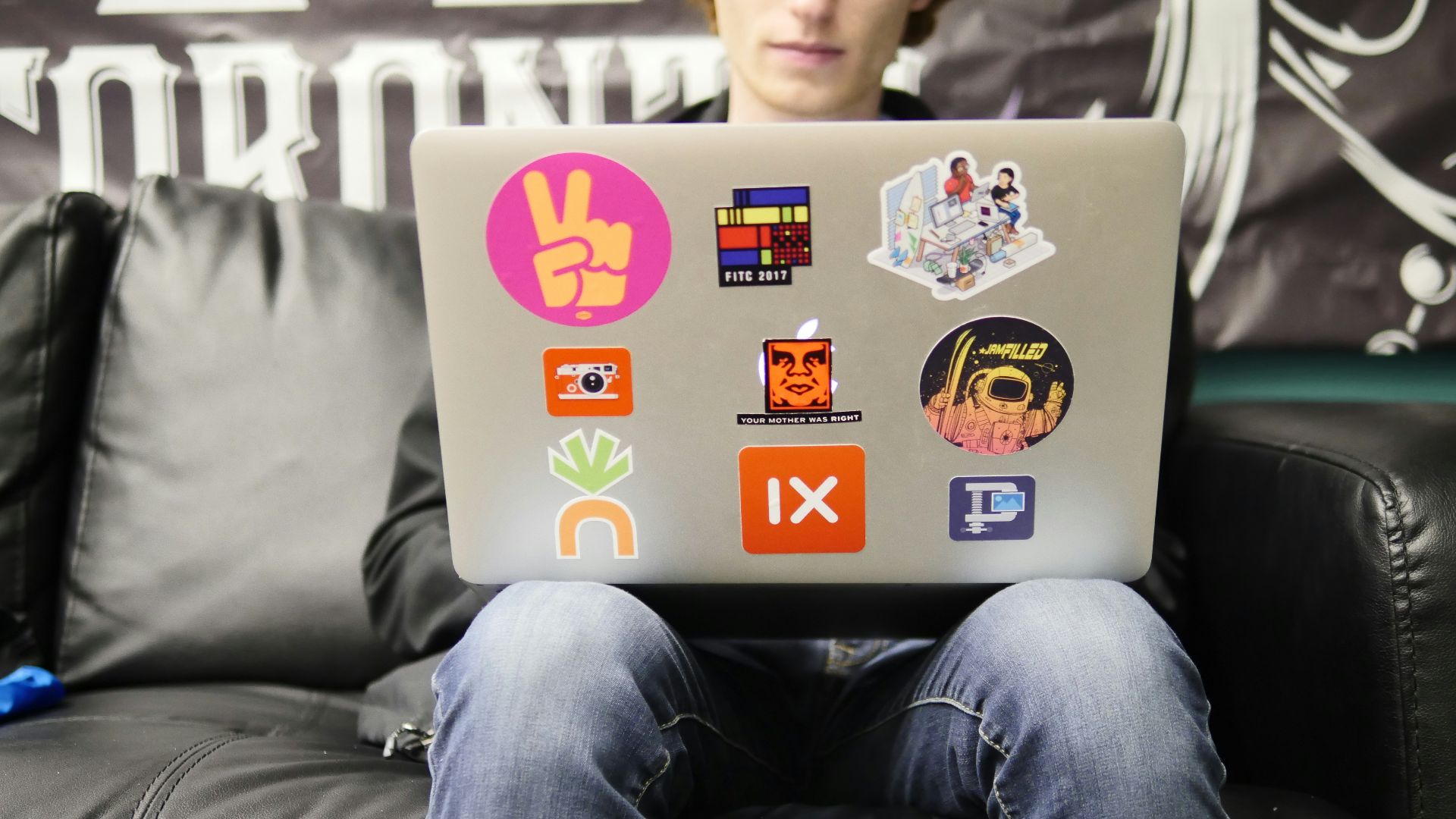 man using silver MacBook sitting on black leather sofa