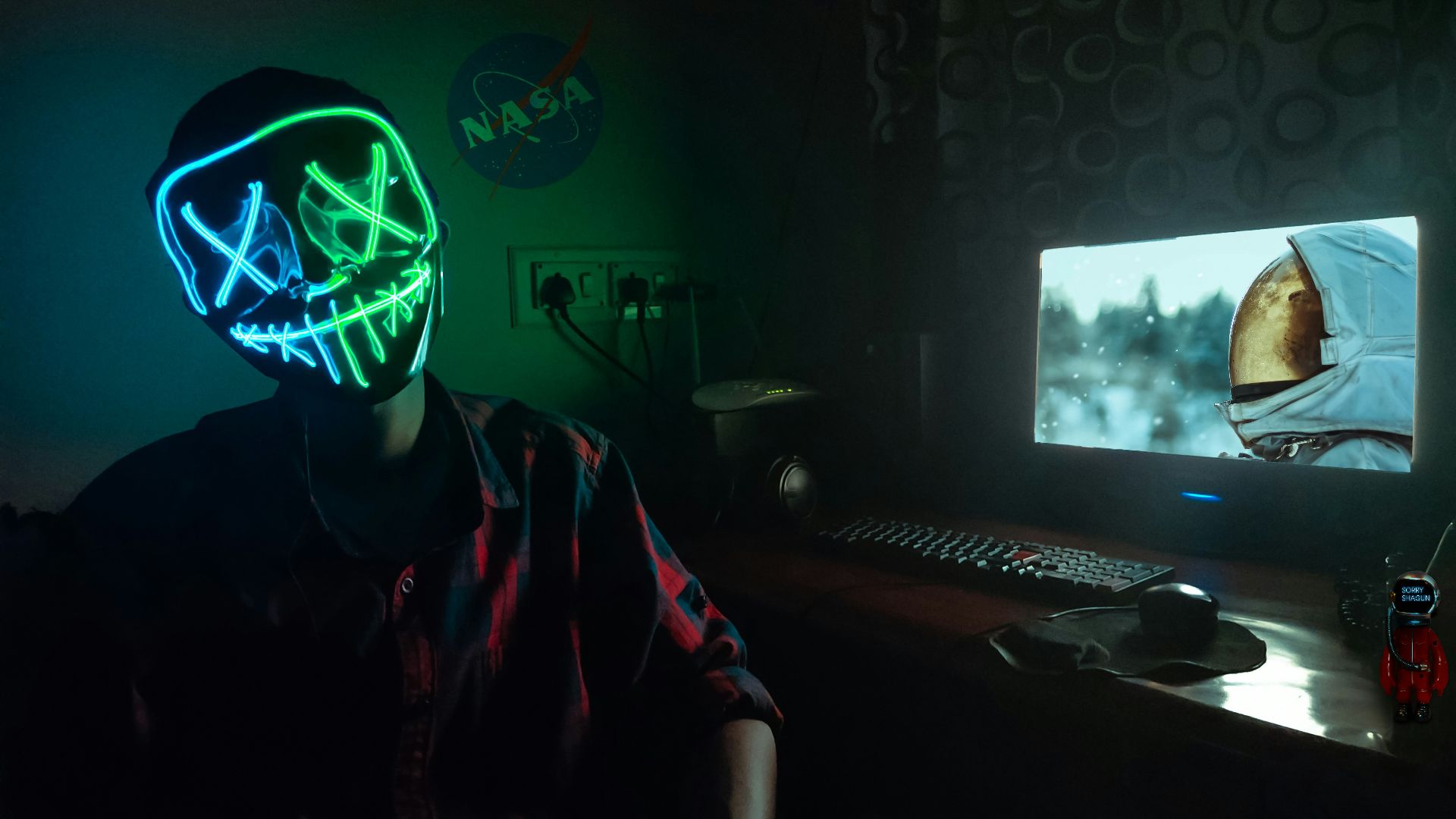 person in blue and green LEd mask sitting in front of turned-on computer monitor