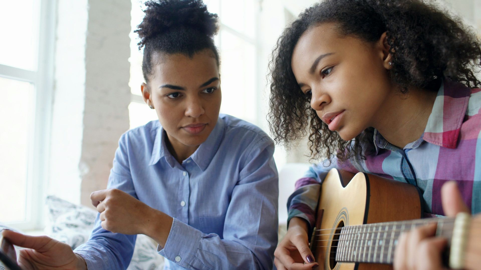 Two young women learning to play guitar together.