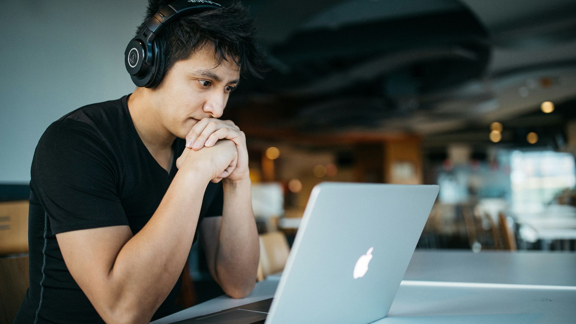 man wearing headphones while sitting on chair in front of MacBook