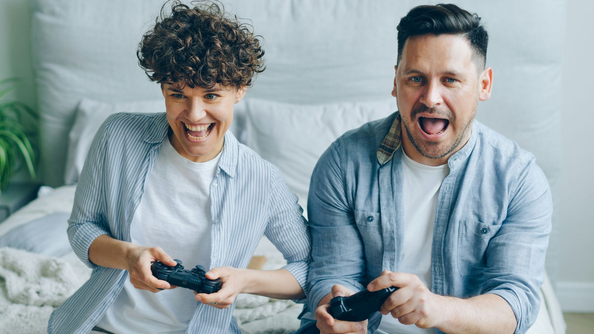 a man and a woman sitting on a bed playing a video game