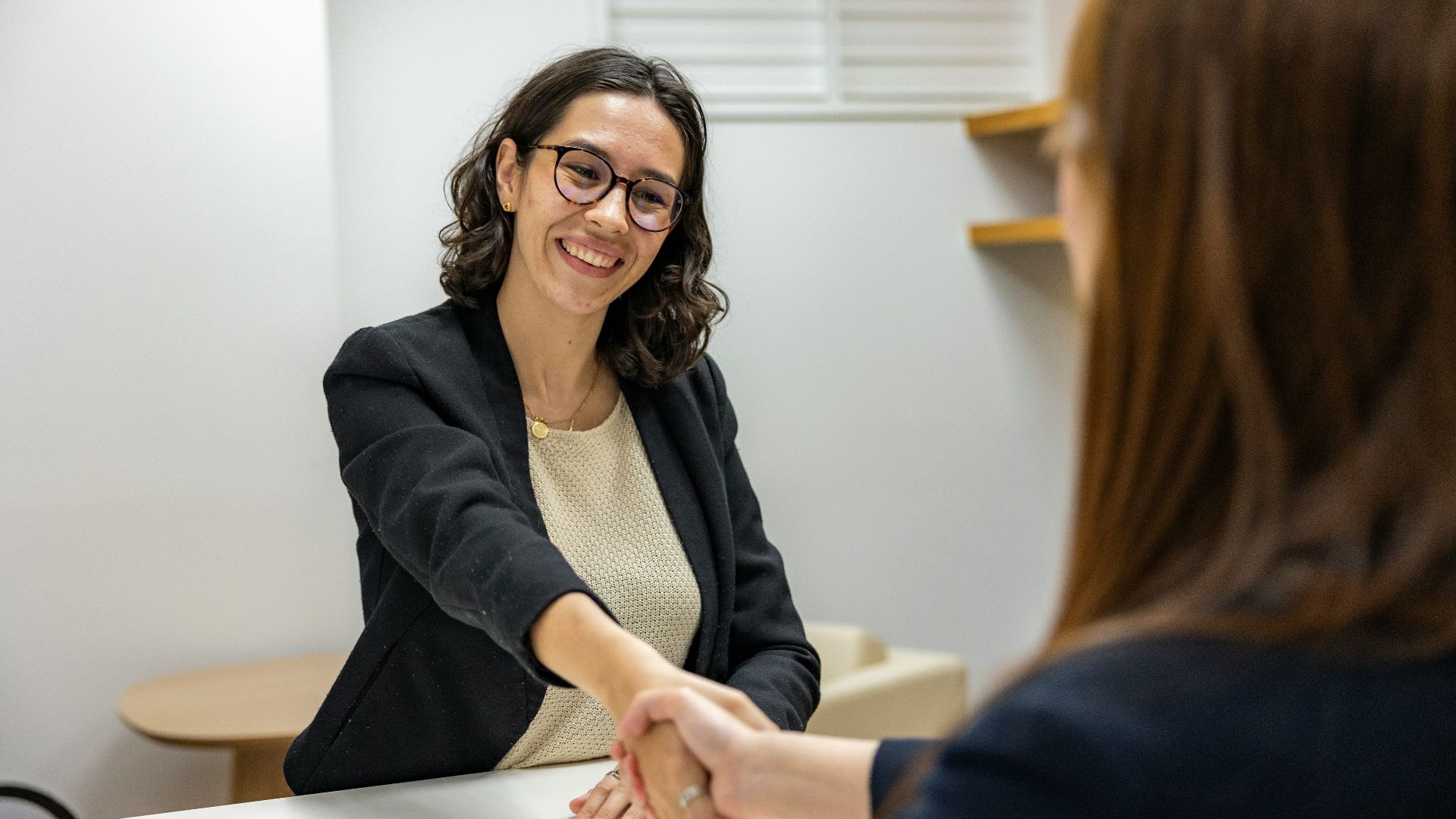 a woman shaking hands with another woman sitting at a table