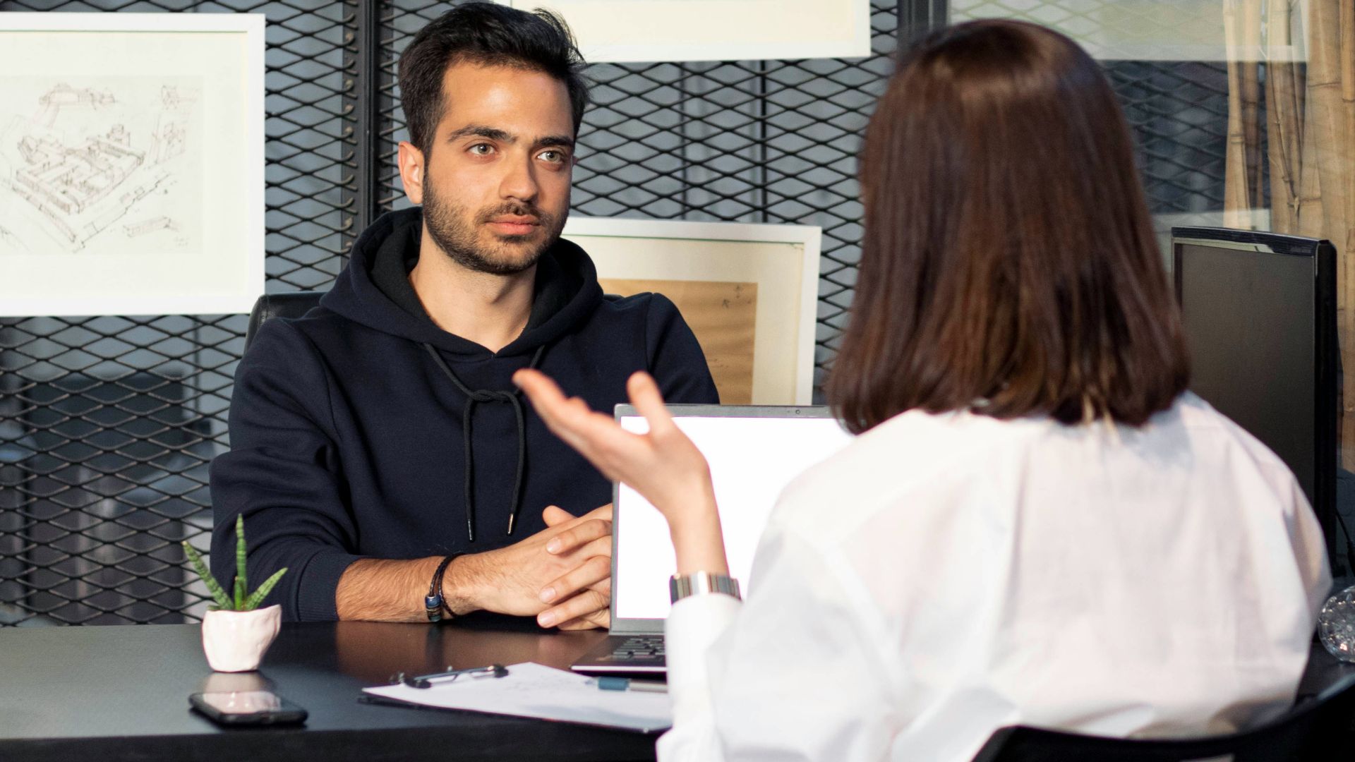 a man sitting at a desk talking to a woman