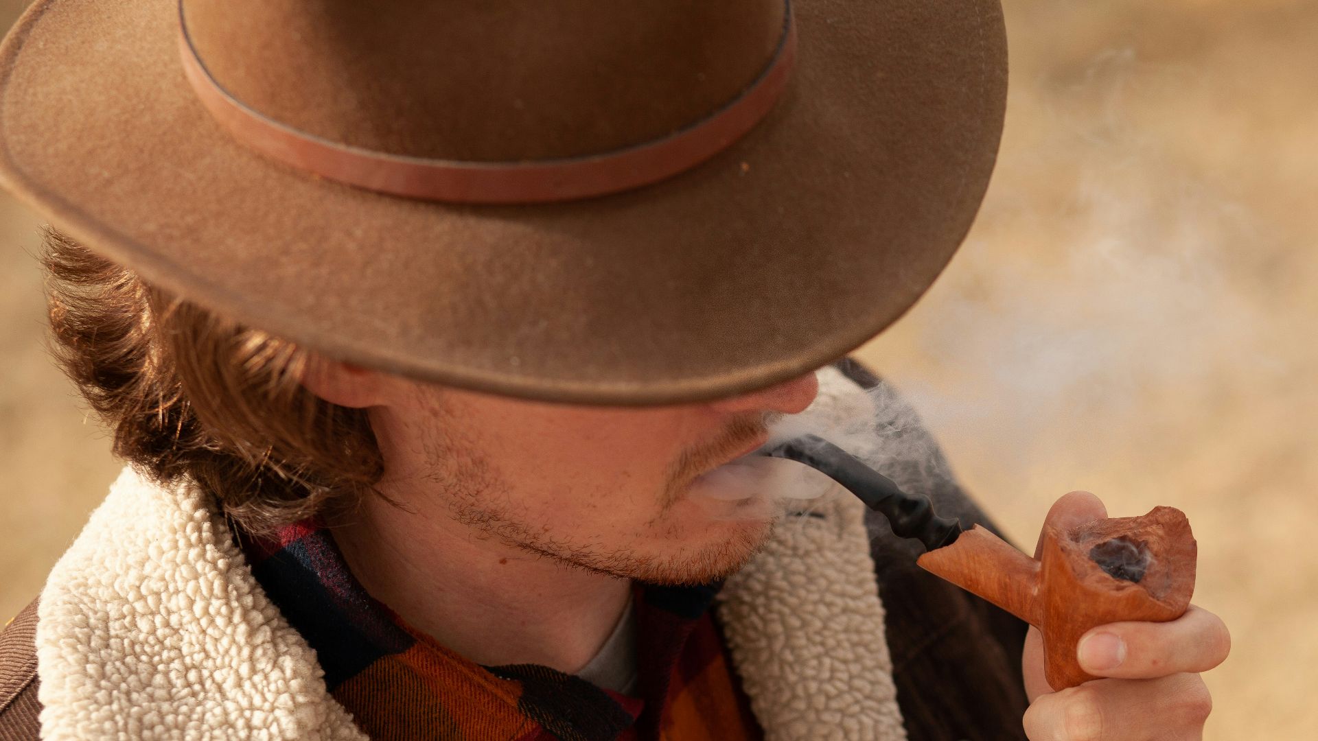 man wearing brown hat and jacket smoking tobacco pipe