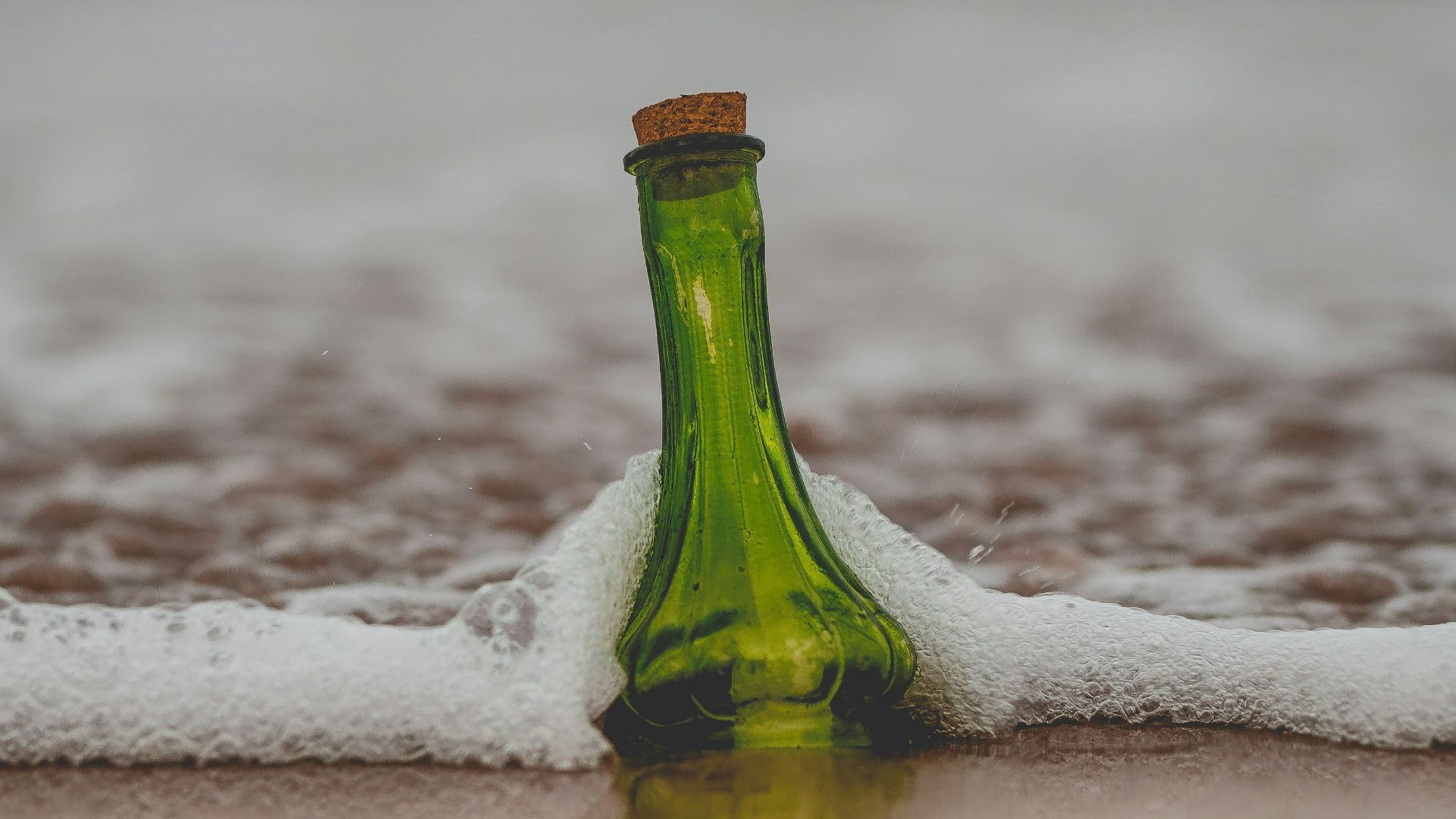 green glass bottle with cork lid on shore
