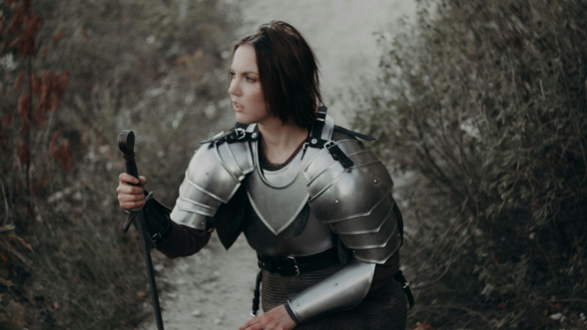 a woman dressed as a knight kneeling on a path