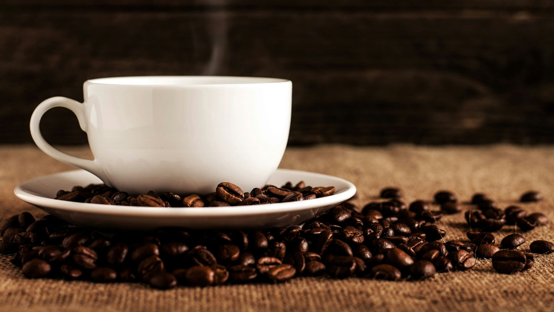 white ceramic mug and saucer with coffee beans on brown textile