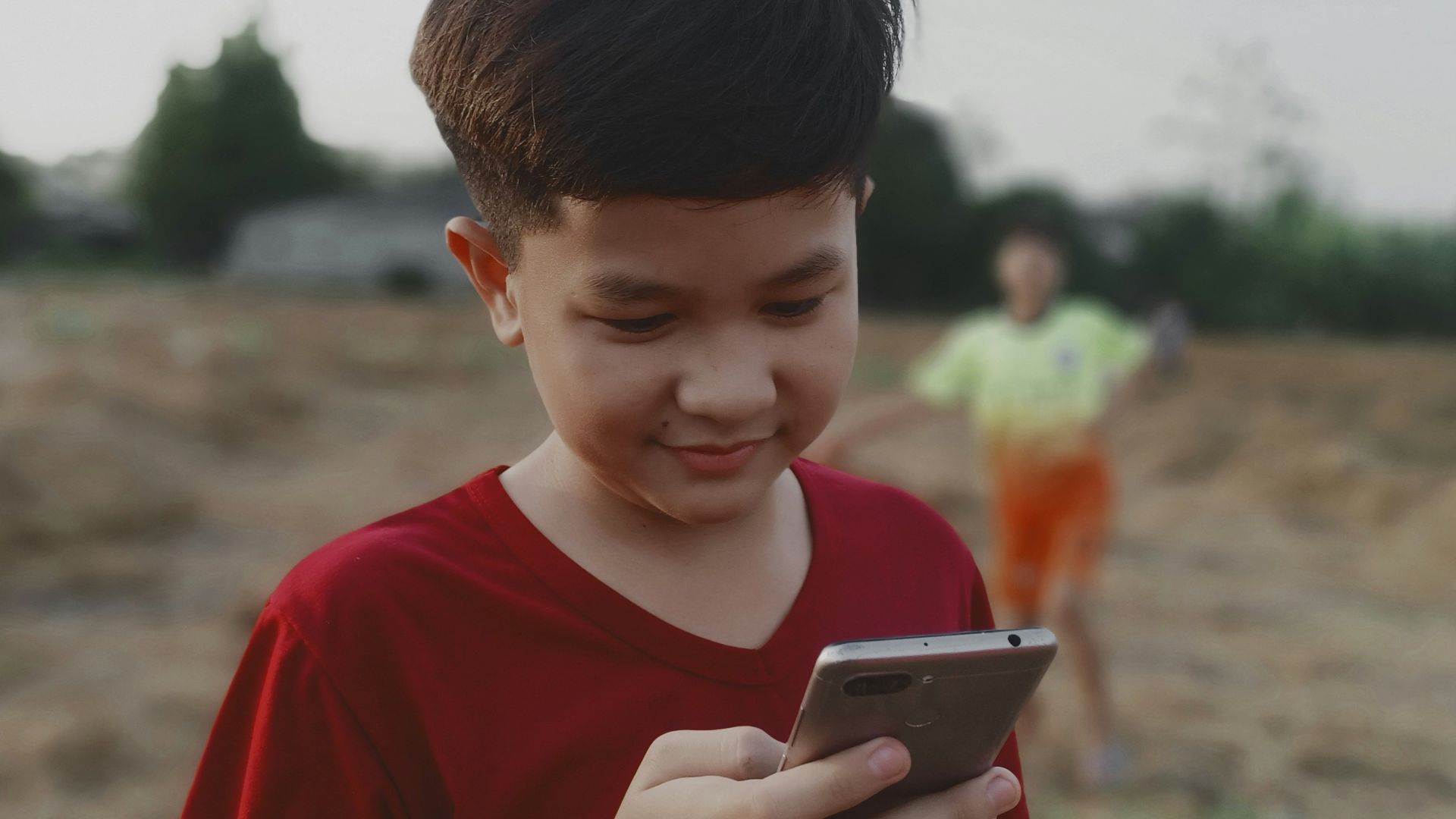 boy in red crew neck shirt holding black smartphone