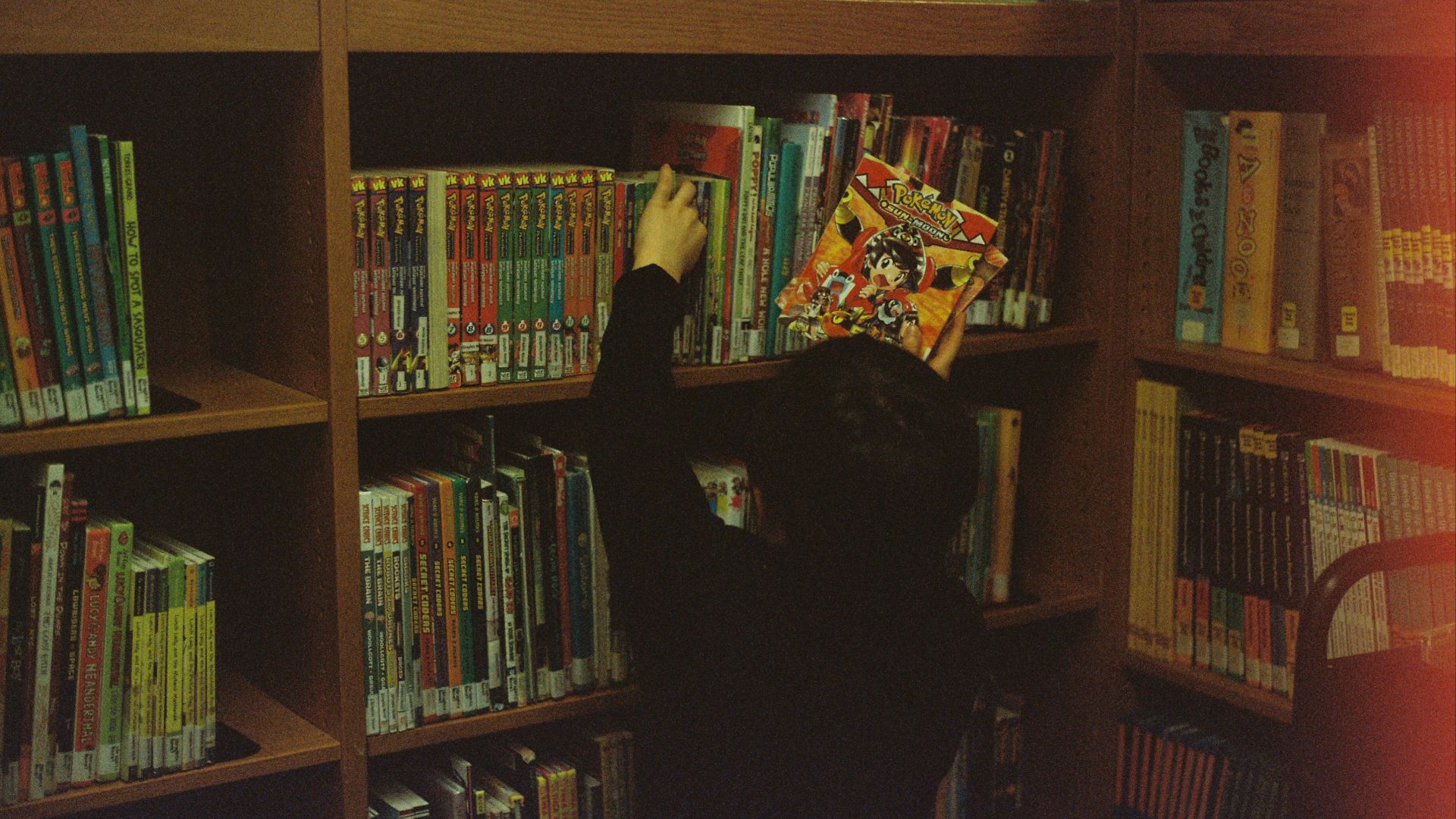 person in black long sleeve shirt standing near brown wooden shelf