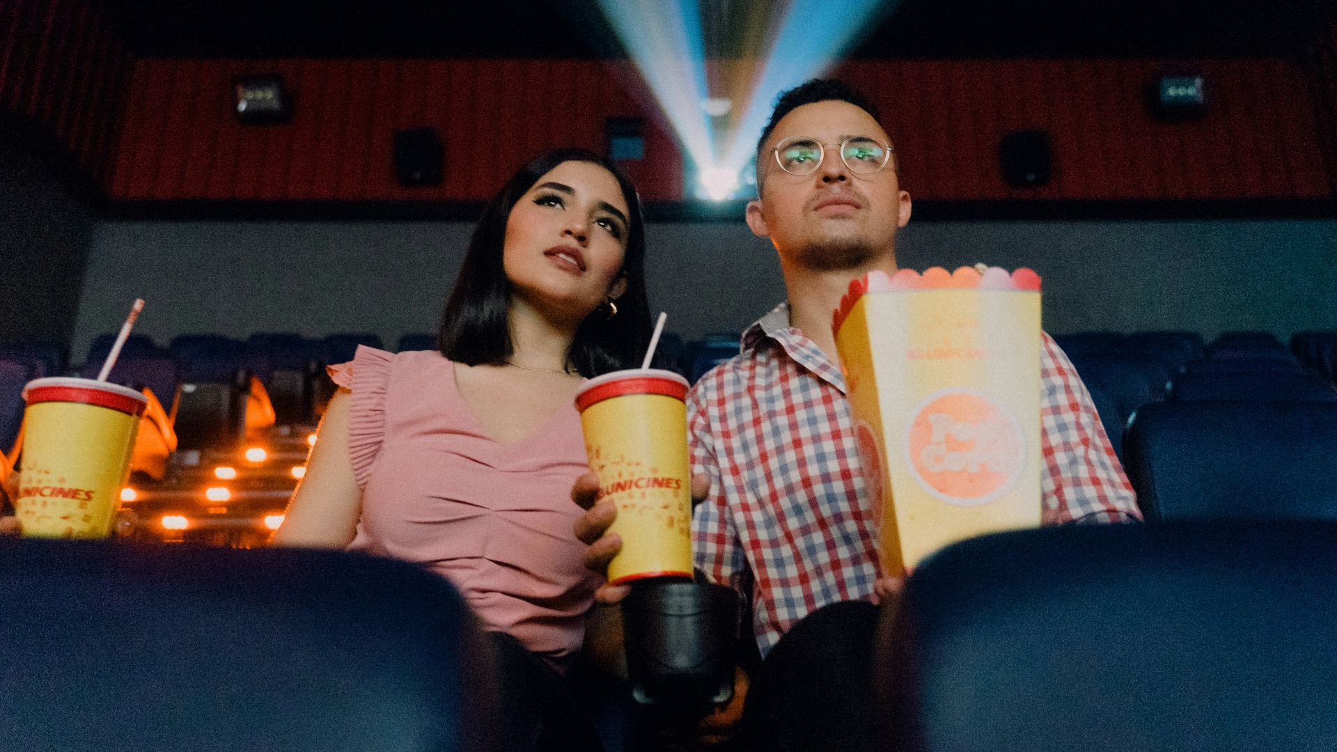2 women sitting on blue leather chair holding white and red plastic cups