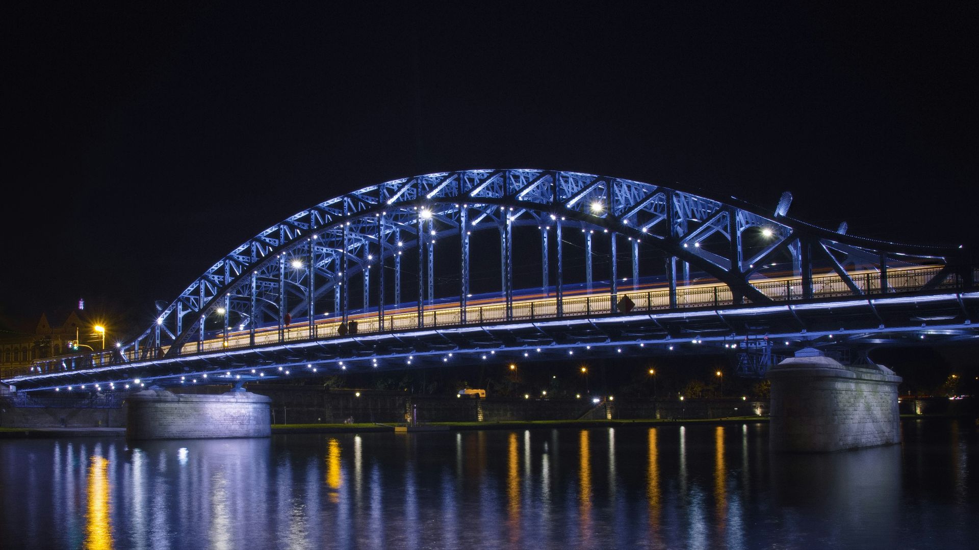 A lit-up bridge shimmers over water at night.