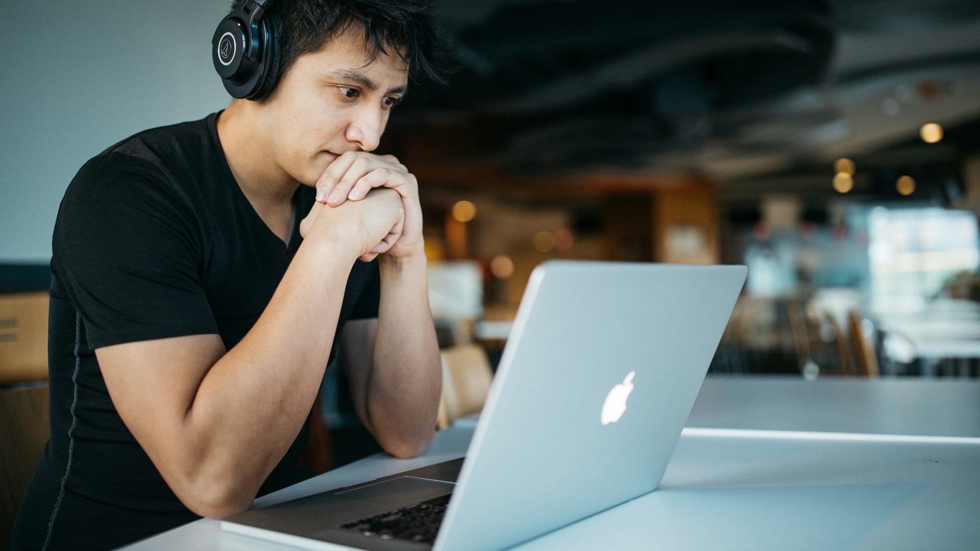 man wearing headphones while sitting on chair in front of MacBook