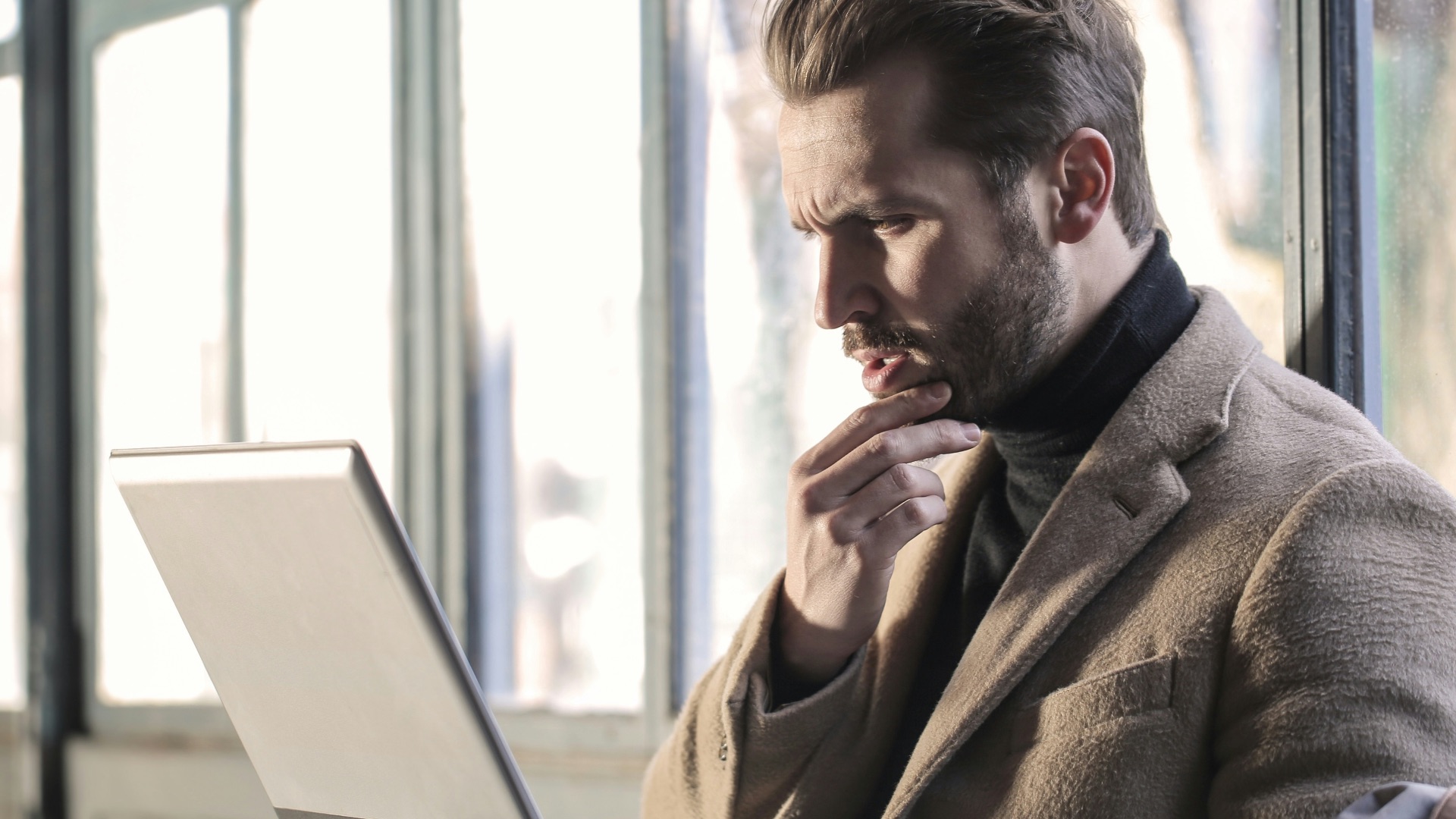 man holding his chin facing laptop computer