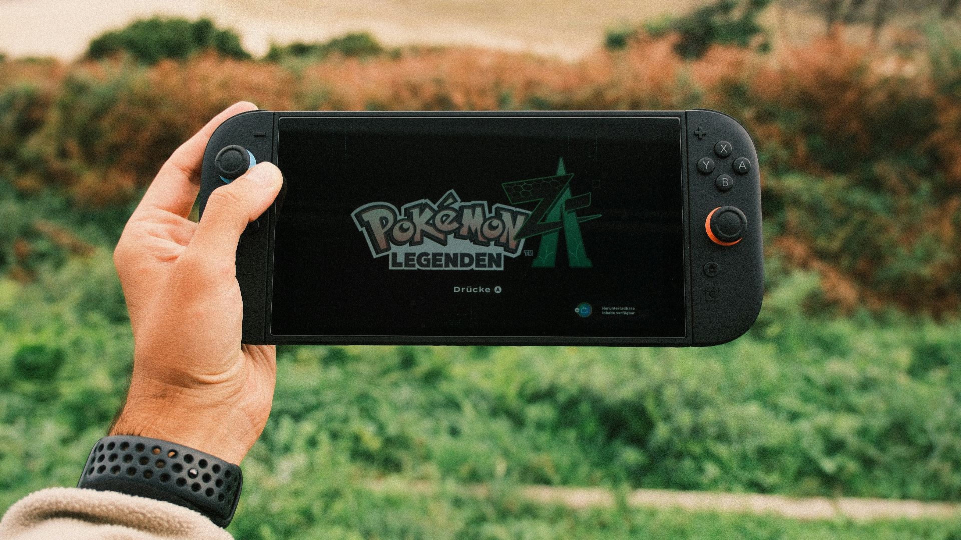 Hand holding gaming device with pokemon legends arceus displayed.