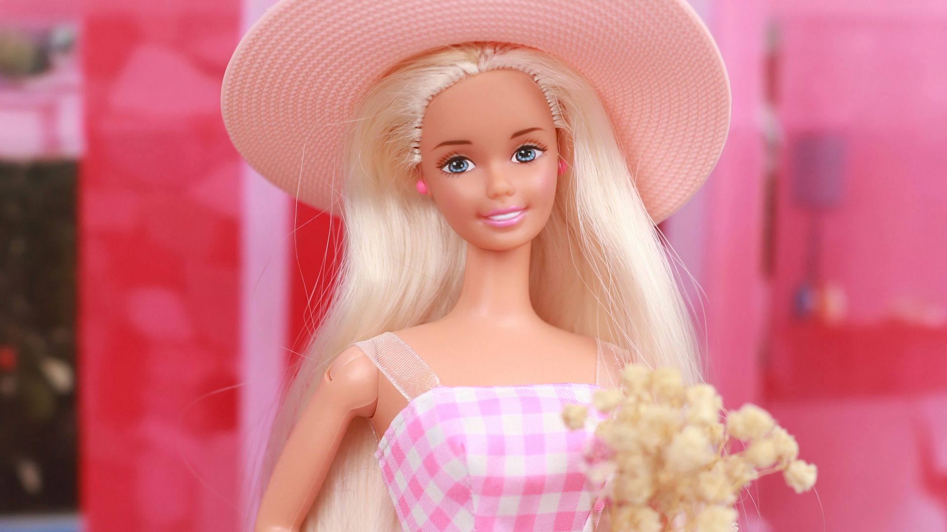 A barbie doll in a pink dress and hat on a pink motorcycle