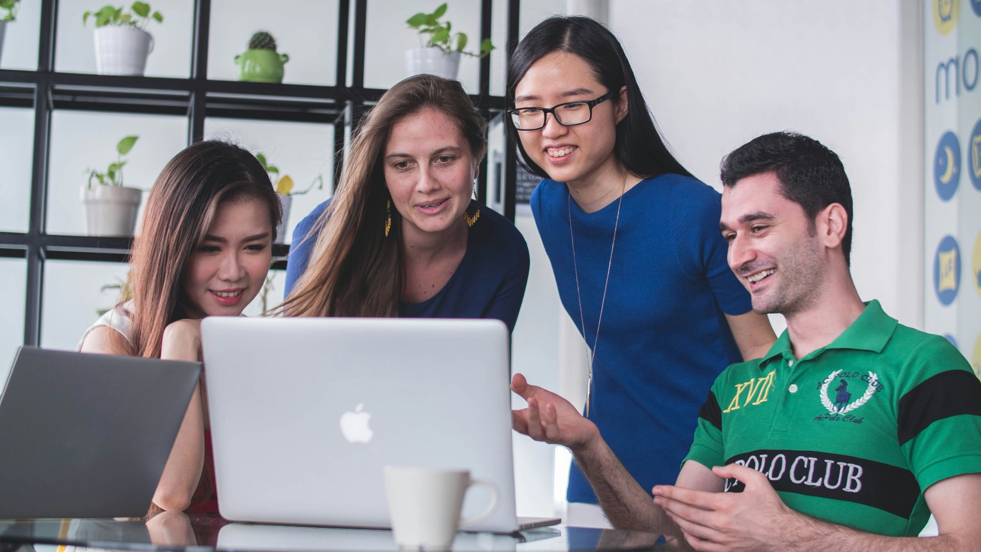 four people watching on white MacBook on top of glass-top table