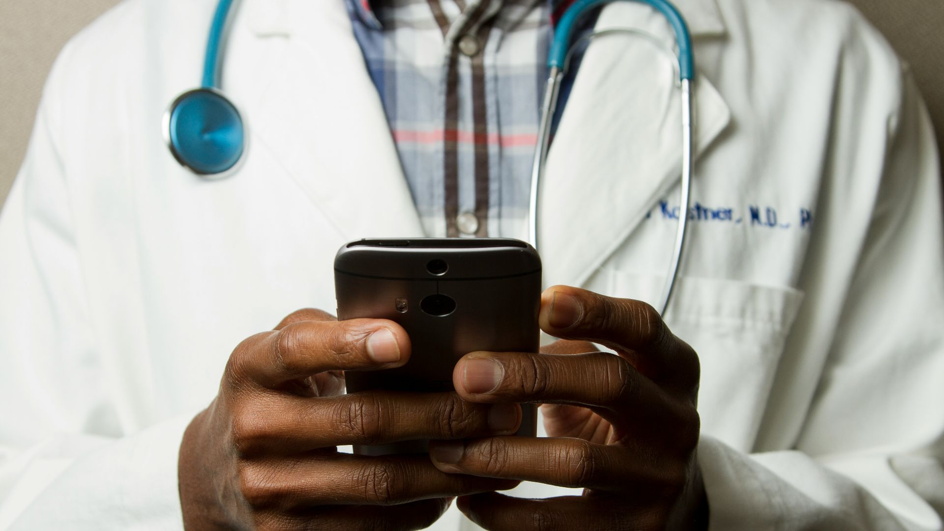 person wearing lavatory gown with green stethoscope on neck using phone while standing