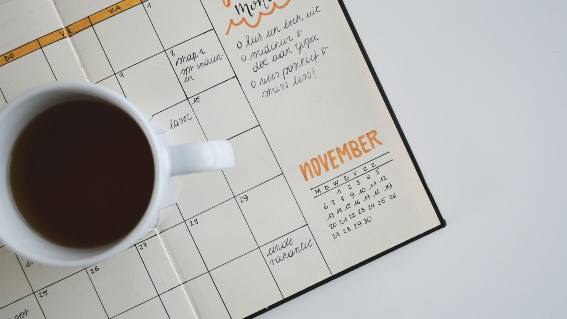 white ceramic mug with coffee on top of a planner