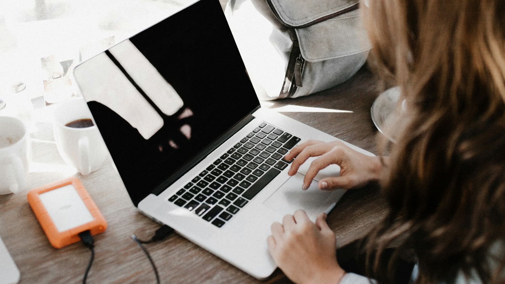 girl wearing grey long-sleeved shirt using MacBook Pro on brown wooden table