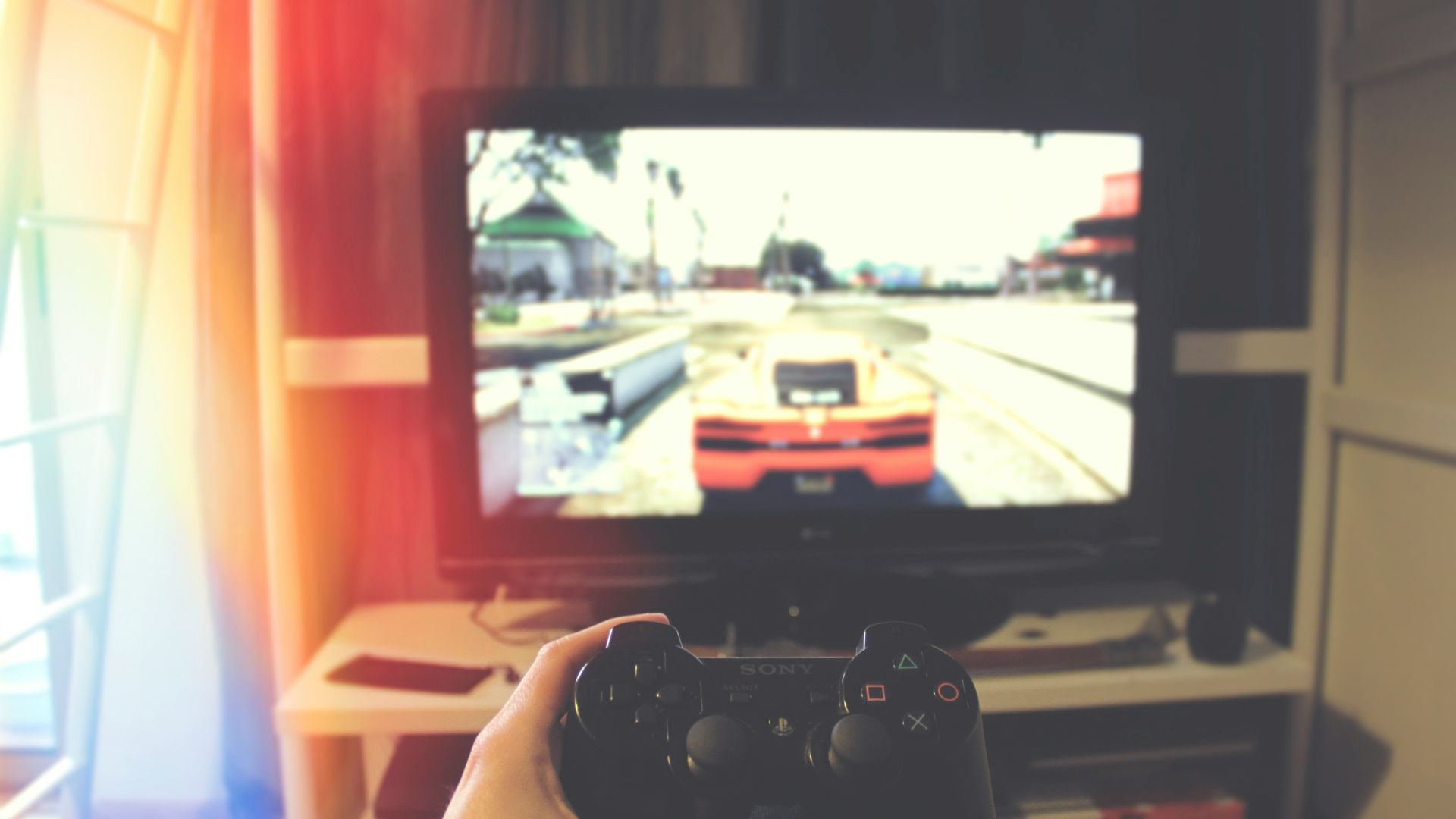 person holding Sony PS3 controller in front of flat screen monitor