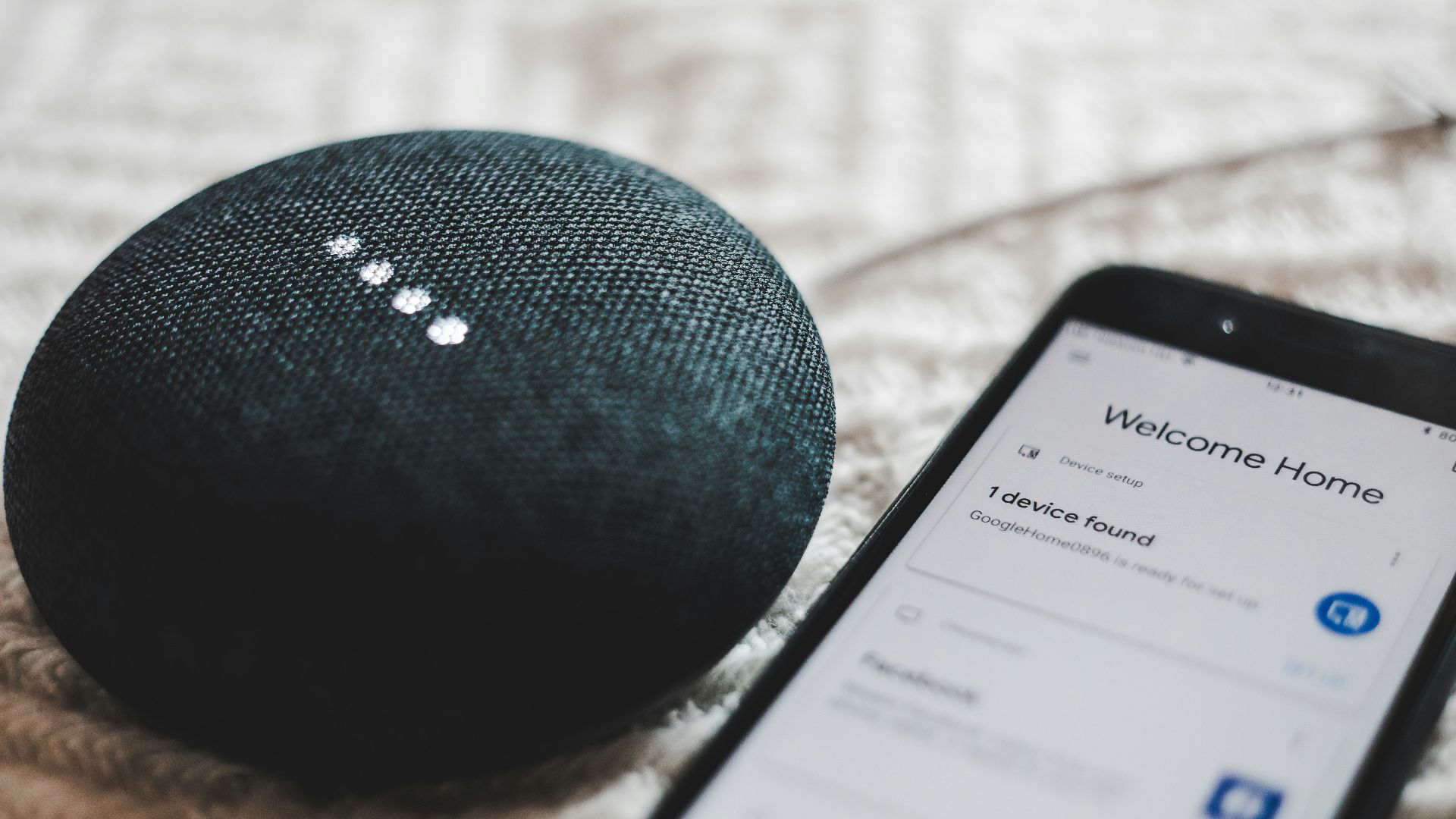 turned-on charcoal Google Home Mini and smartphone