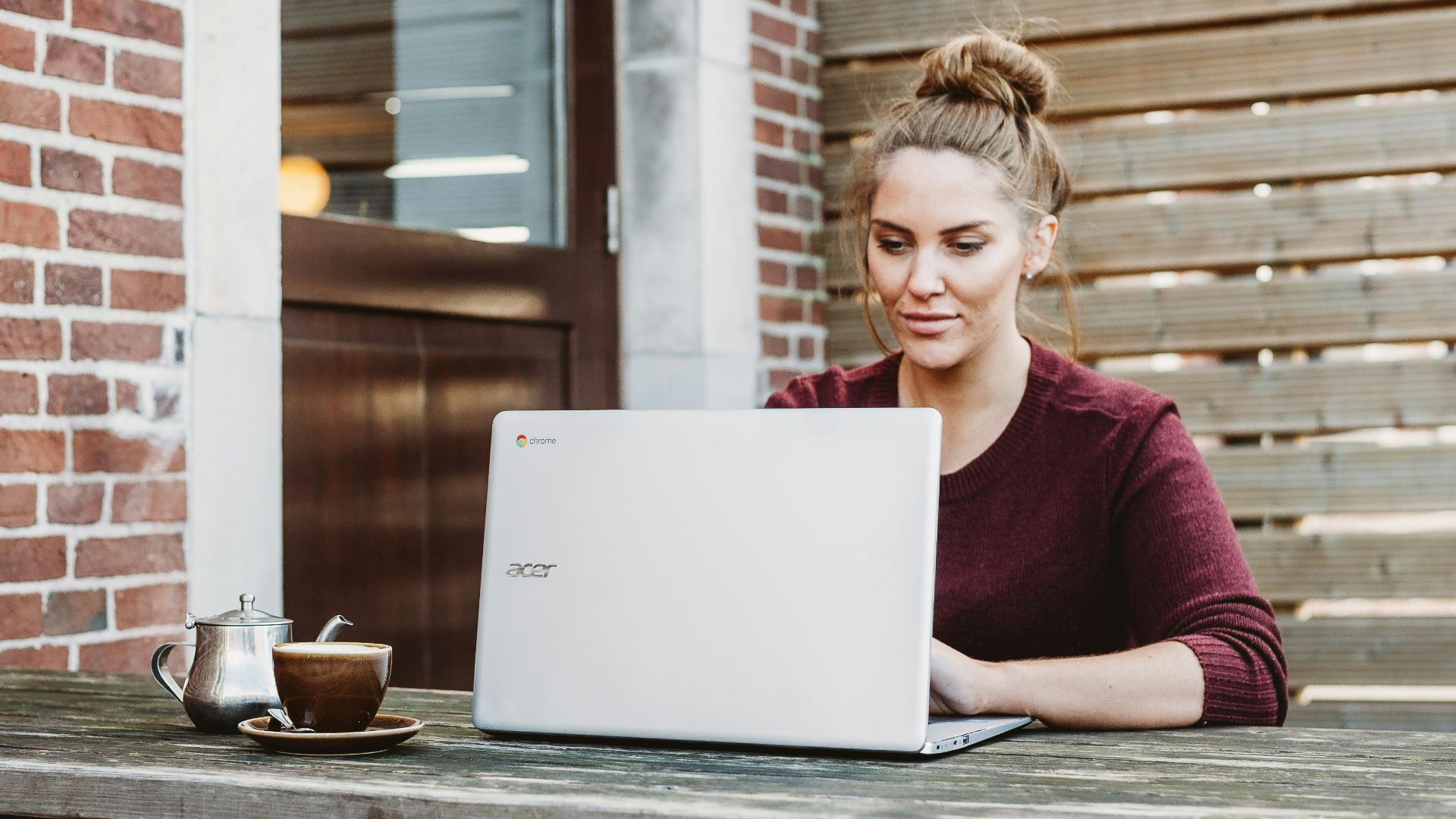 woman sitting and holding white Acer laptop near brown wooden wall