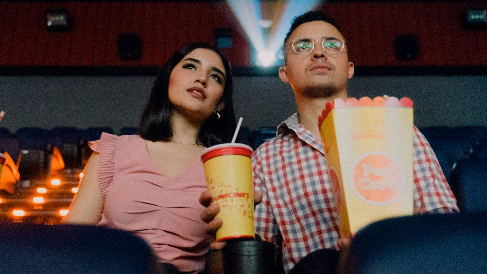2 women sitting on blue leather chair holding white and red plastic cups