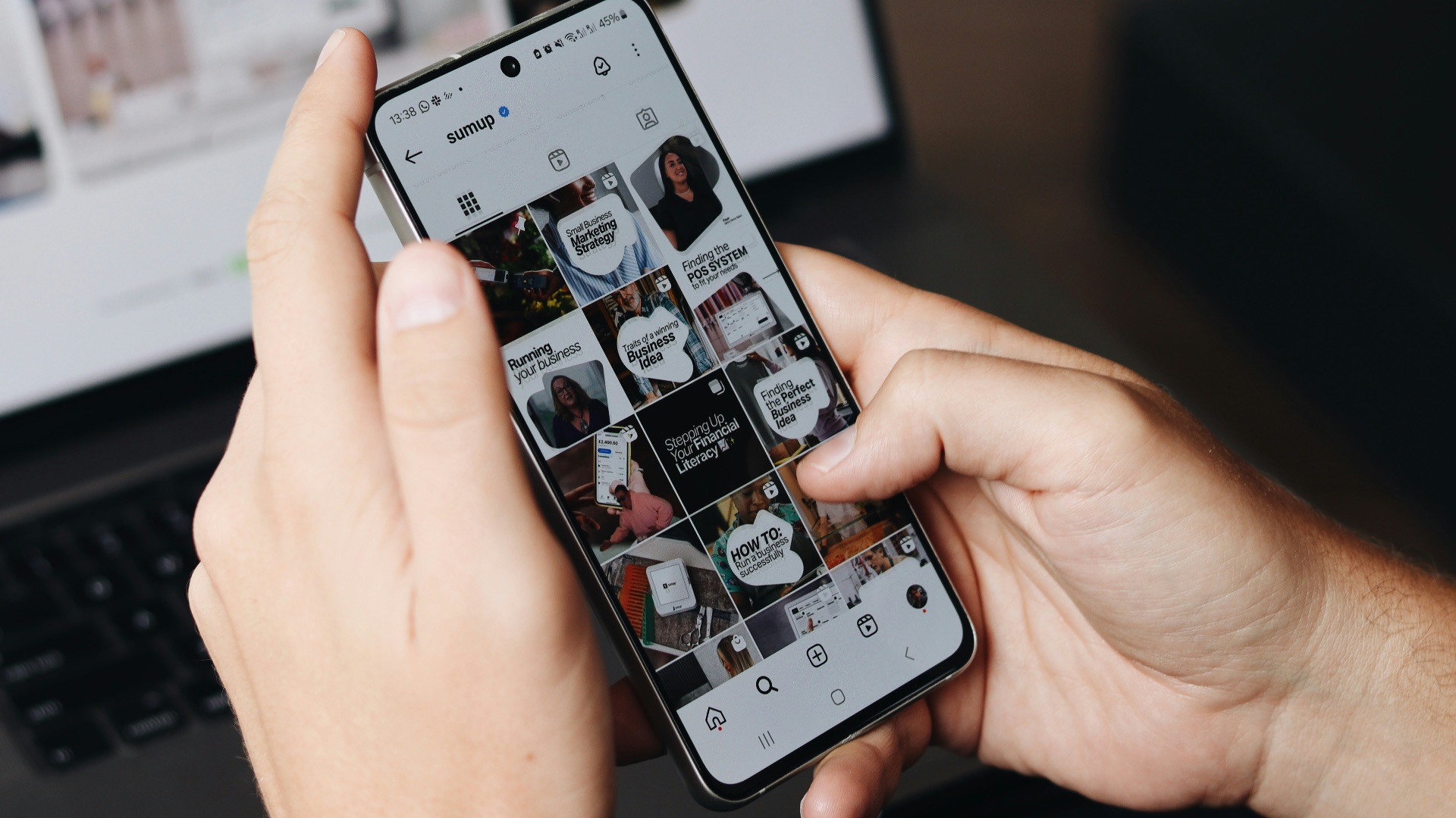 A person holding a cell phone in front of a laptop
