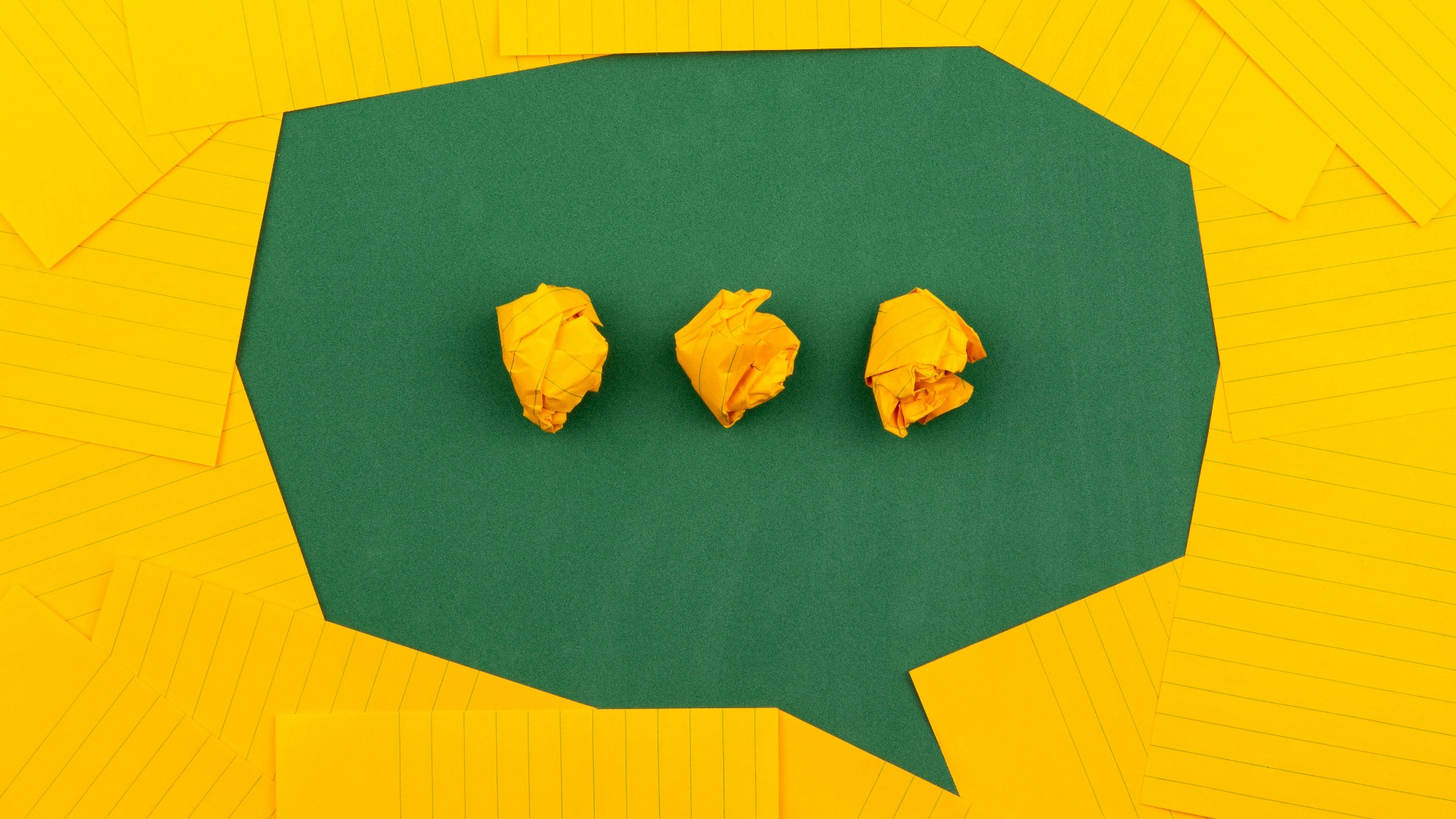 three crumpled yellow papers on green surface surrounded by yellow lined papers