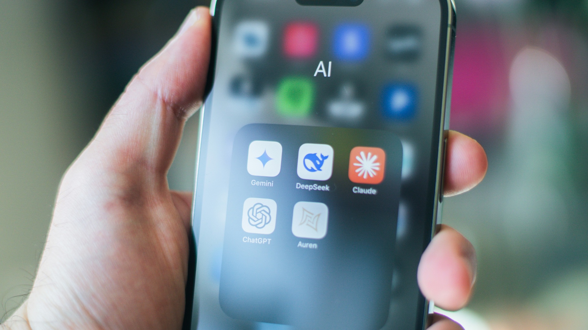 A hand holds a smartphone with various apps.