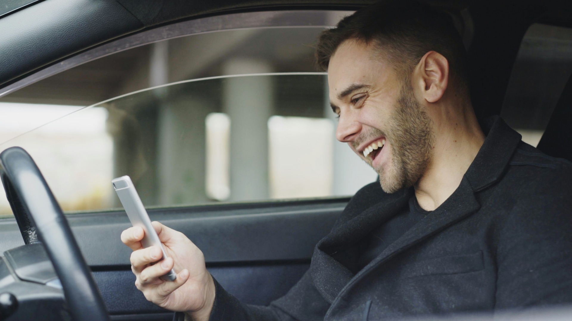 Smiling man looking at his phone in car