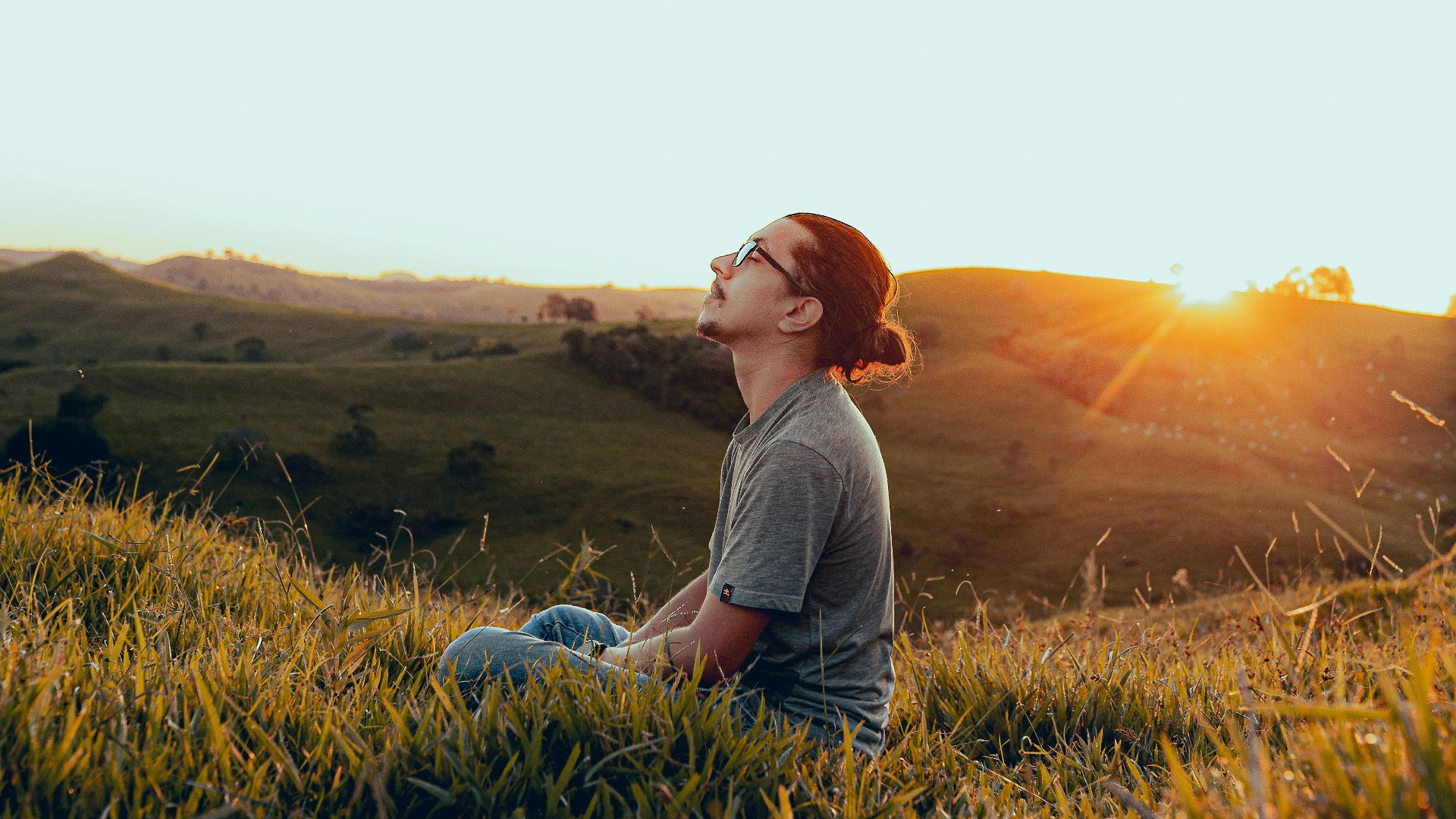 man in white shirt sitting on green grass field during sunset