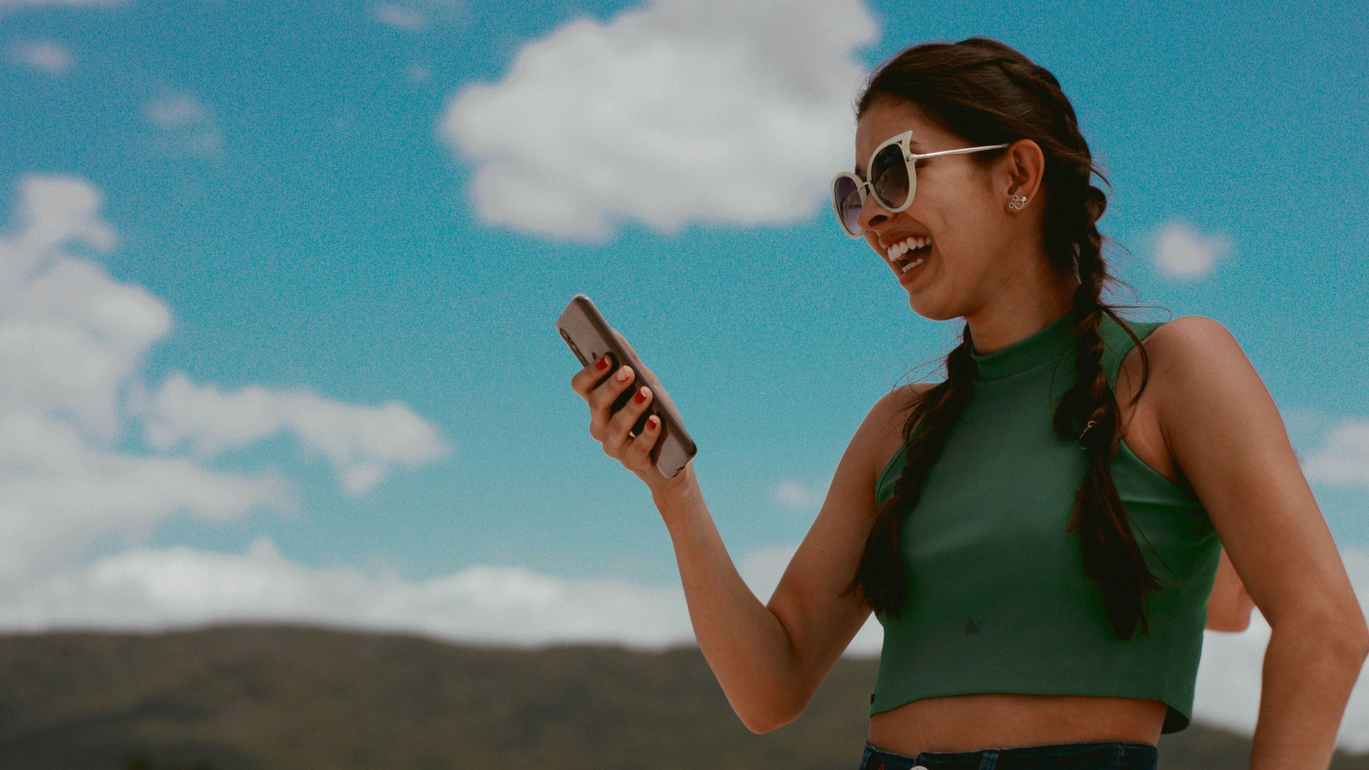 woman in green tank top holding smartphone during daytime