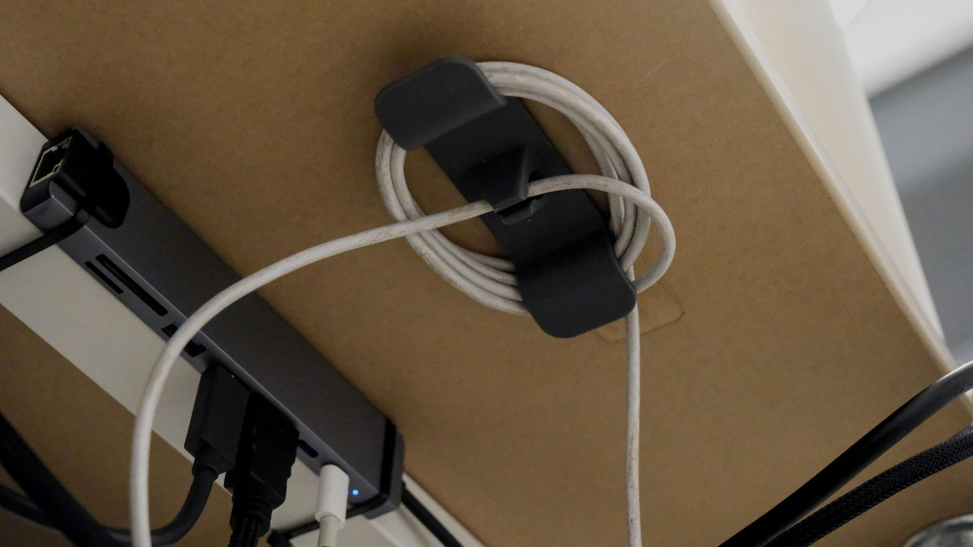Cable organizer holding coiled white cord under desk