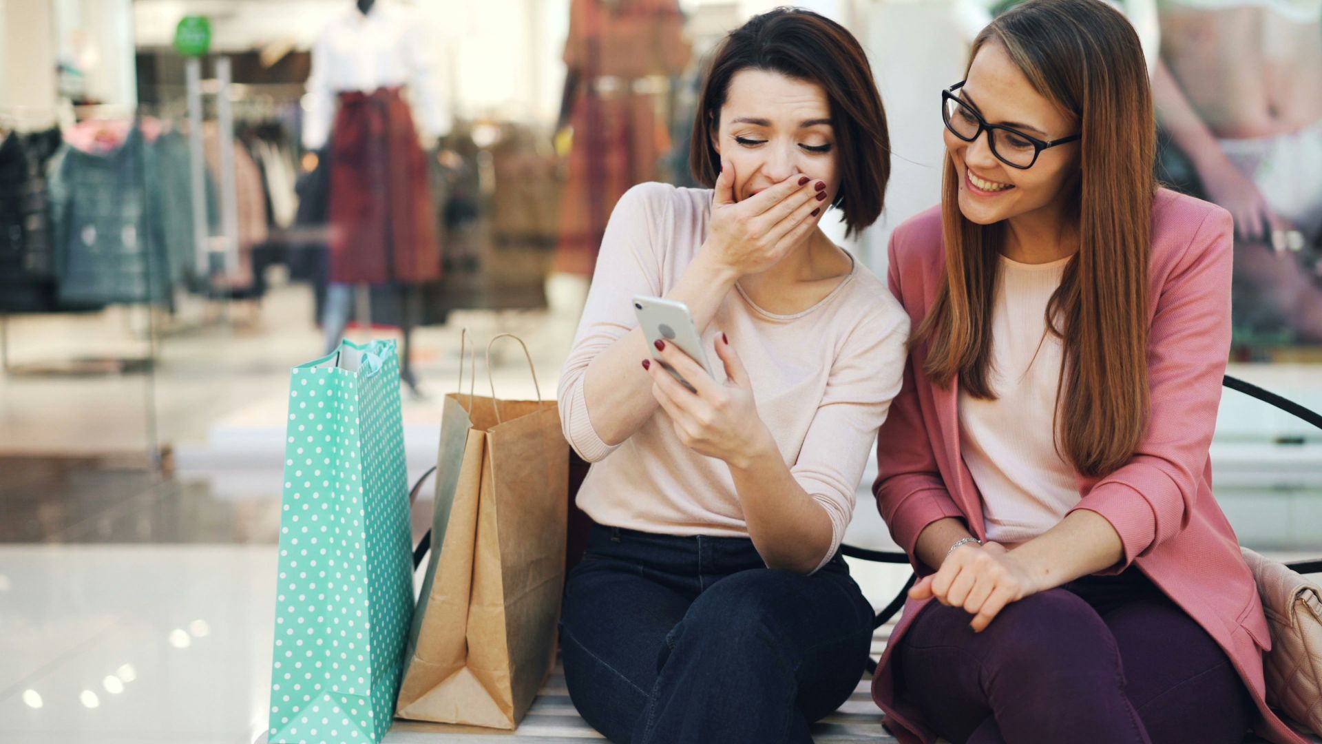 Two women laughing while looking at a smartphone.