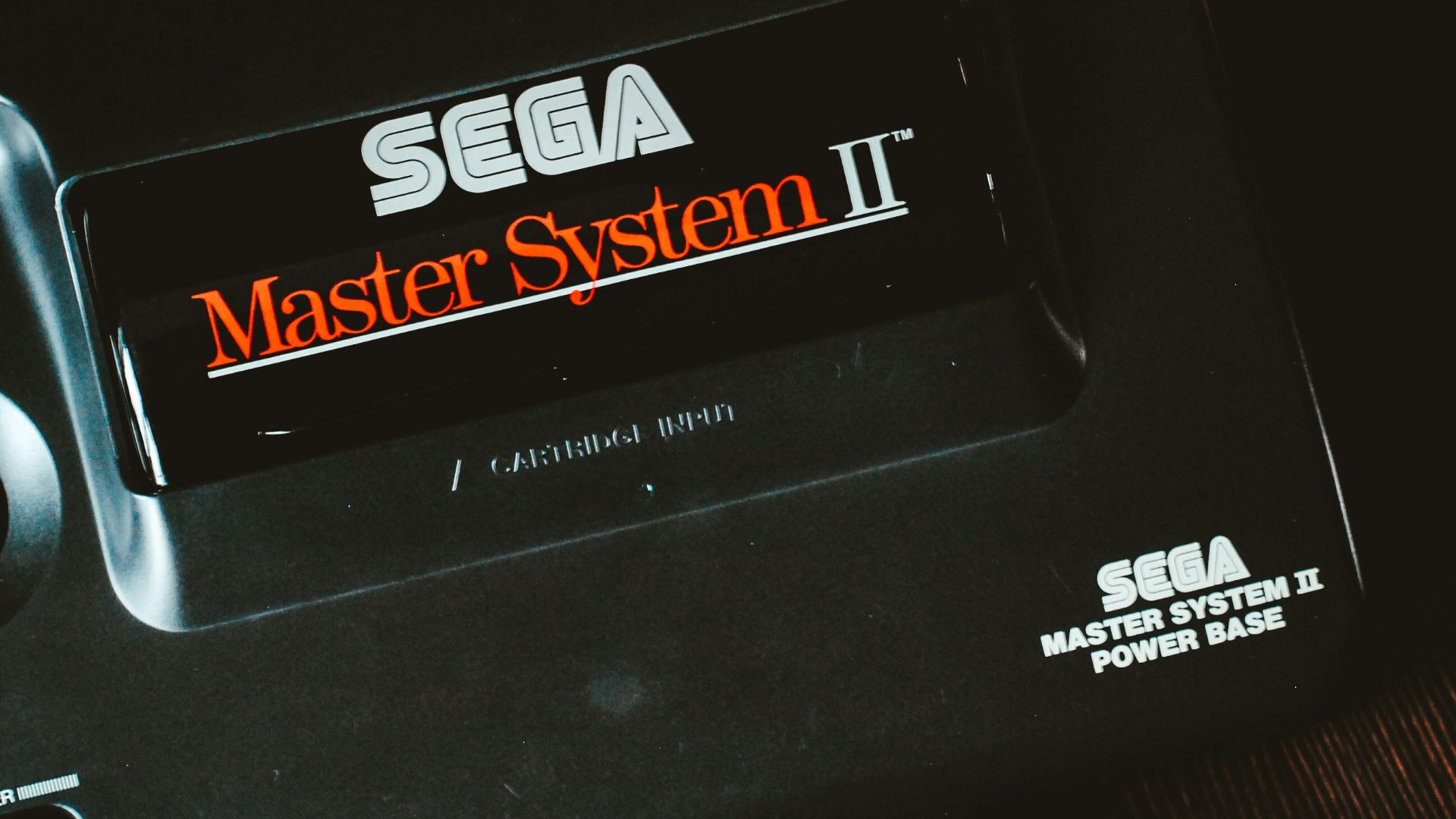 black Sega Master System II device on brown wooden surface