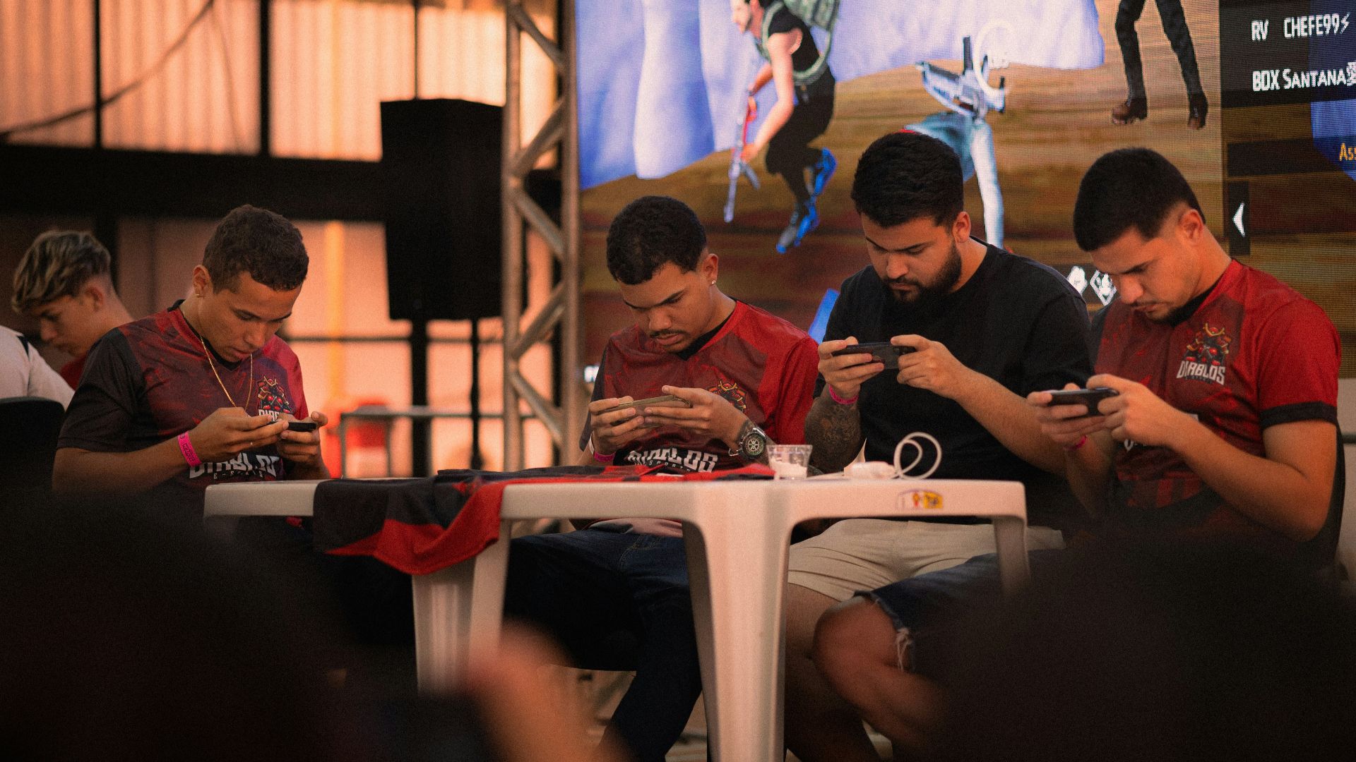 Four men playing mobile games at a table.