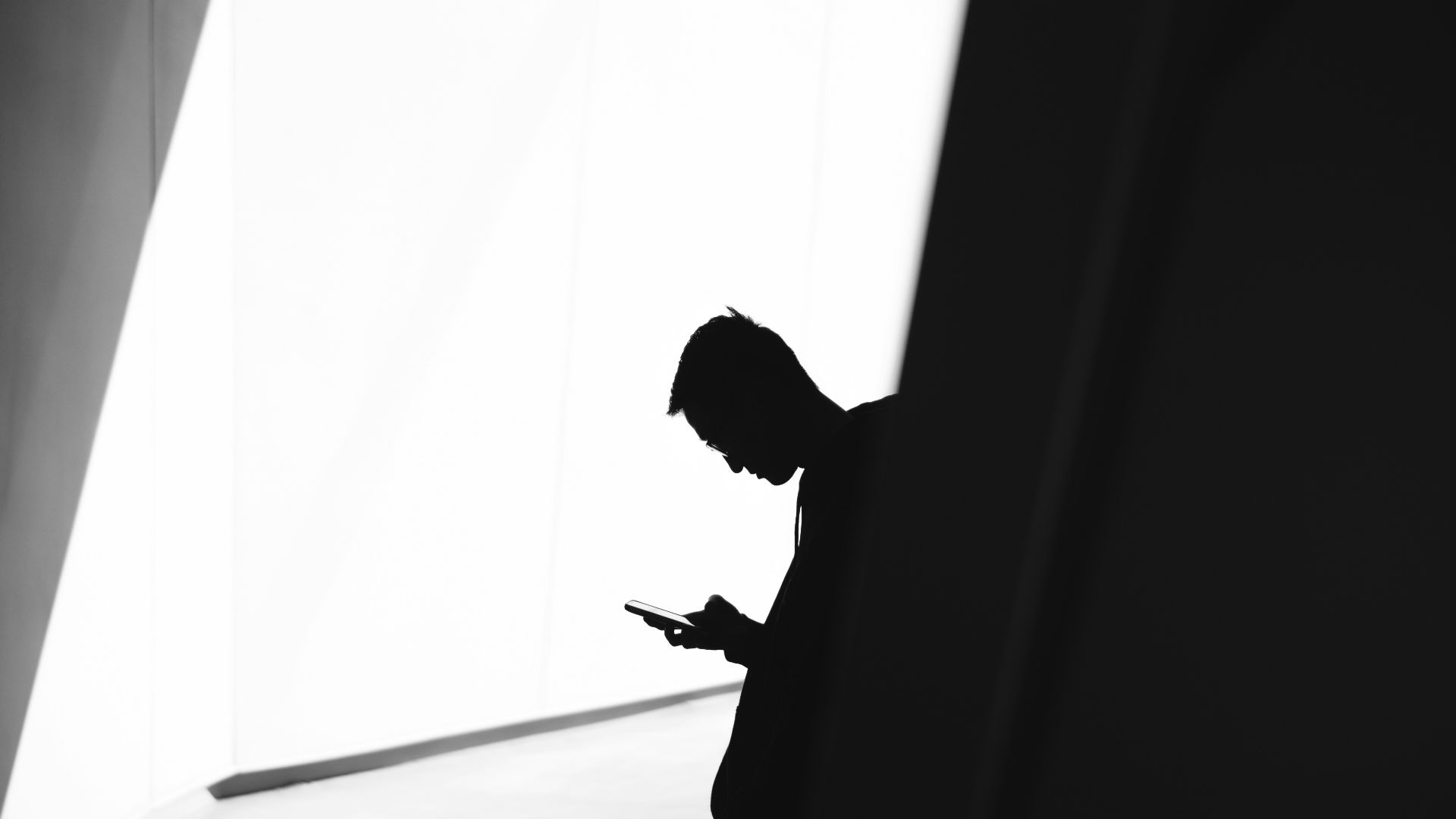 person using phone leaning on wall in silhouette photography