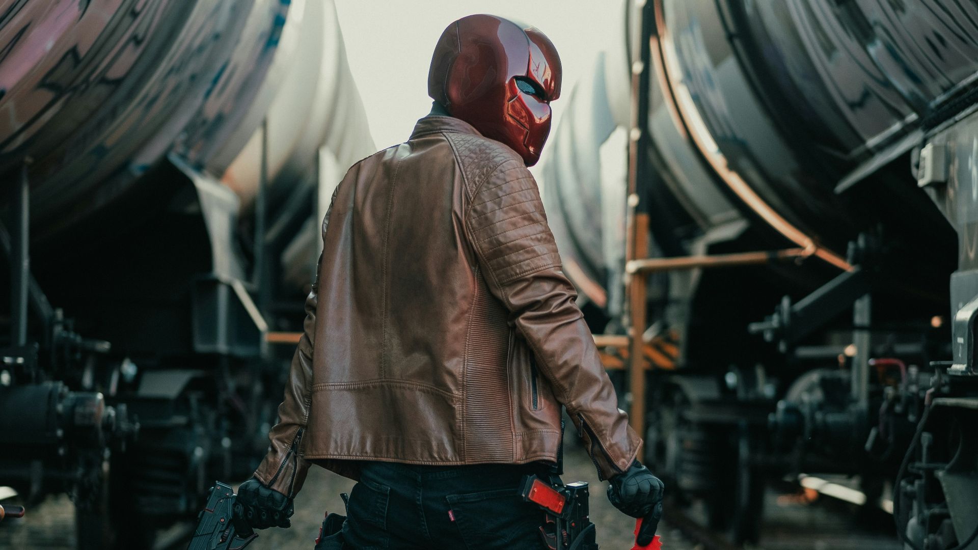 man in brown jacket and black pants standing on train rail during daytime