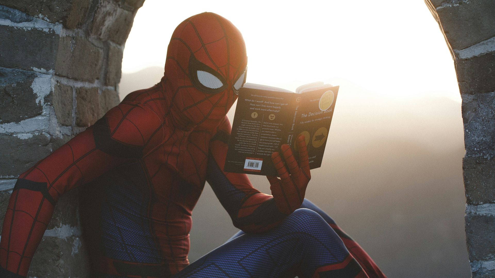 Spider-Man leaning on concrete brick while reading book