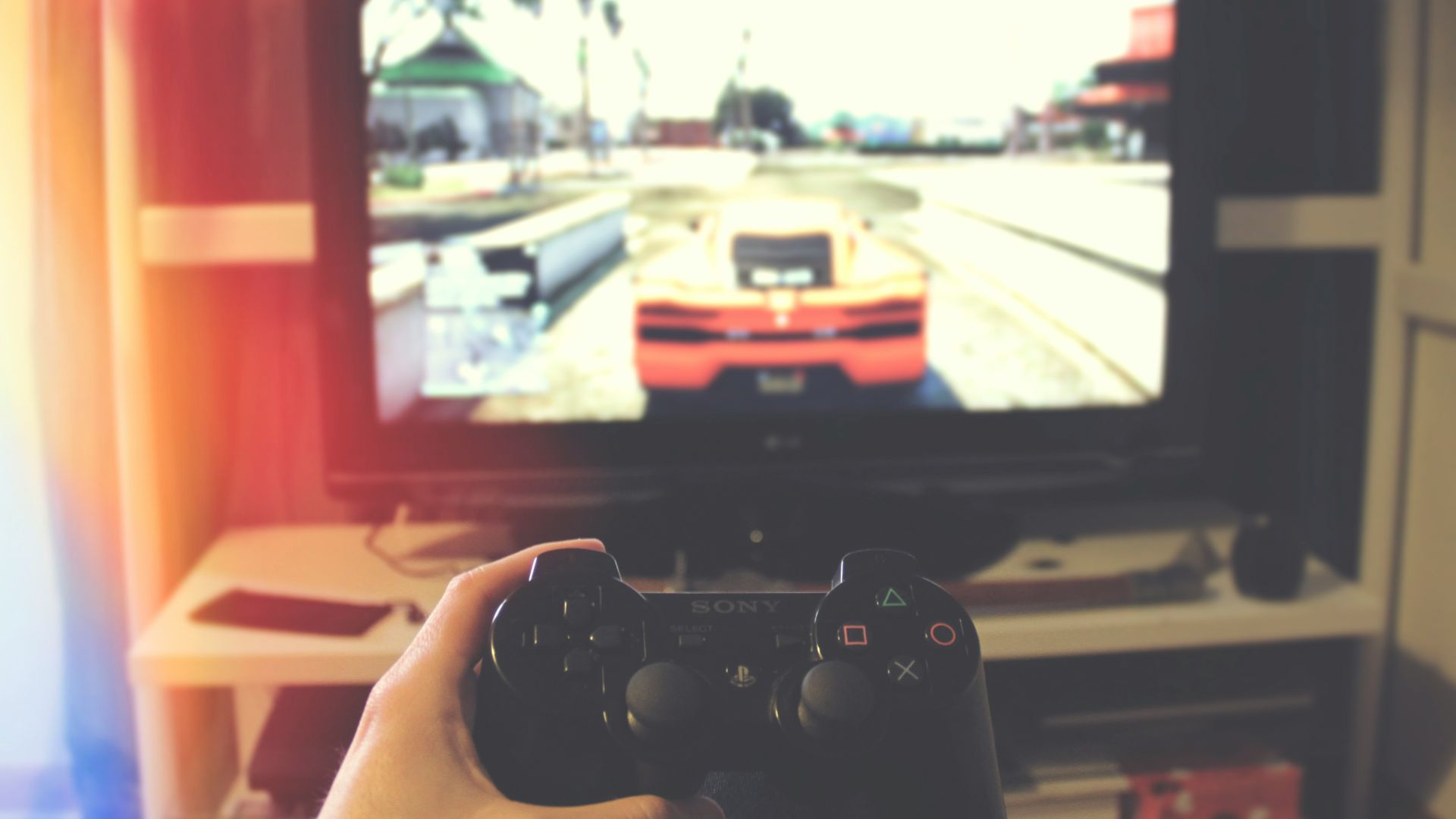 person holding Sony PS3 controller in front of flat screen monitor