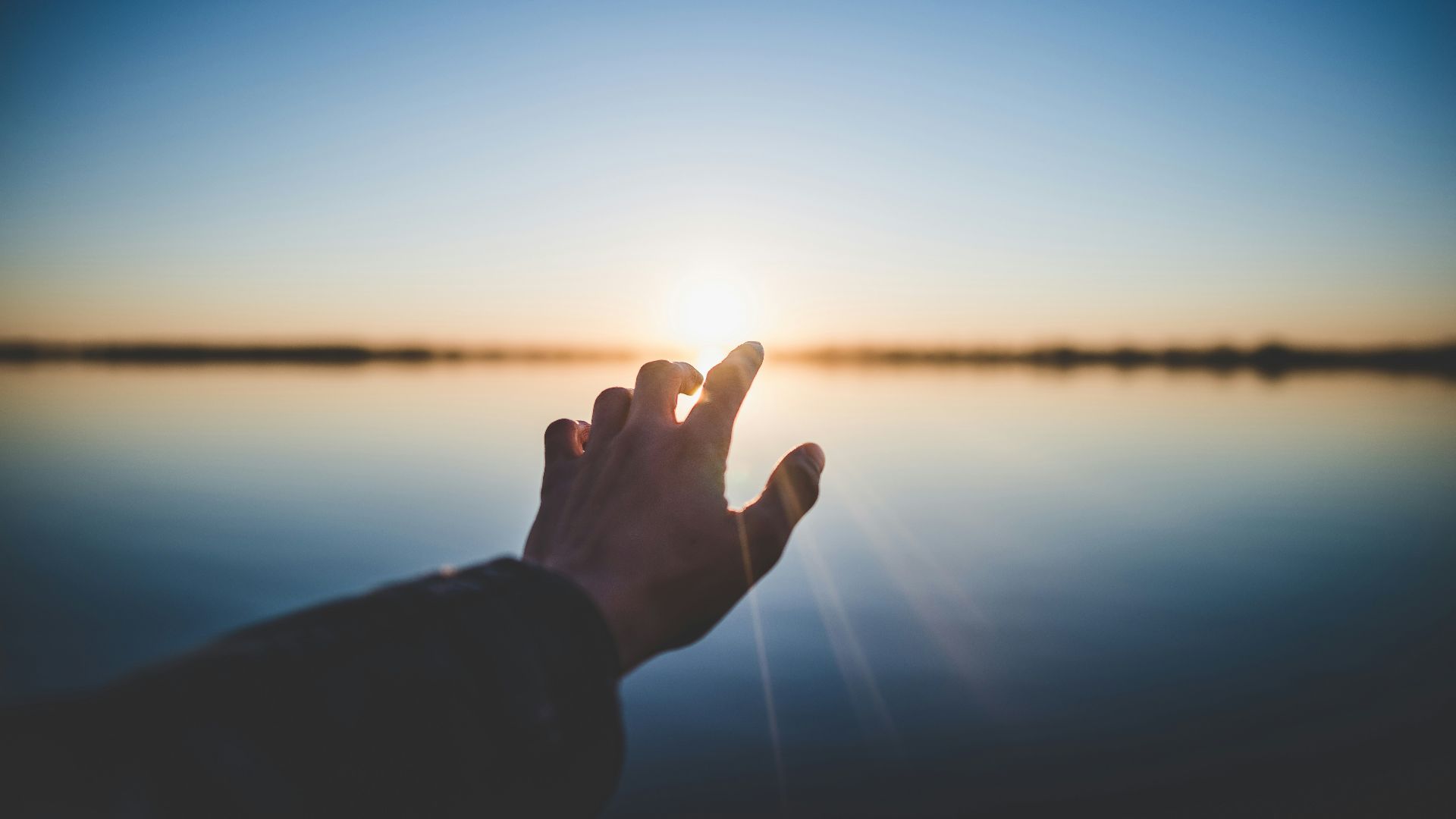landscape photography of person's hand in front of sun